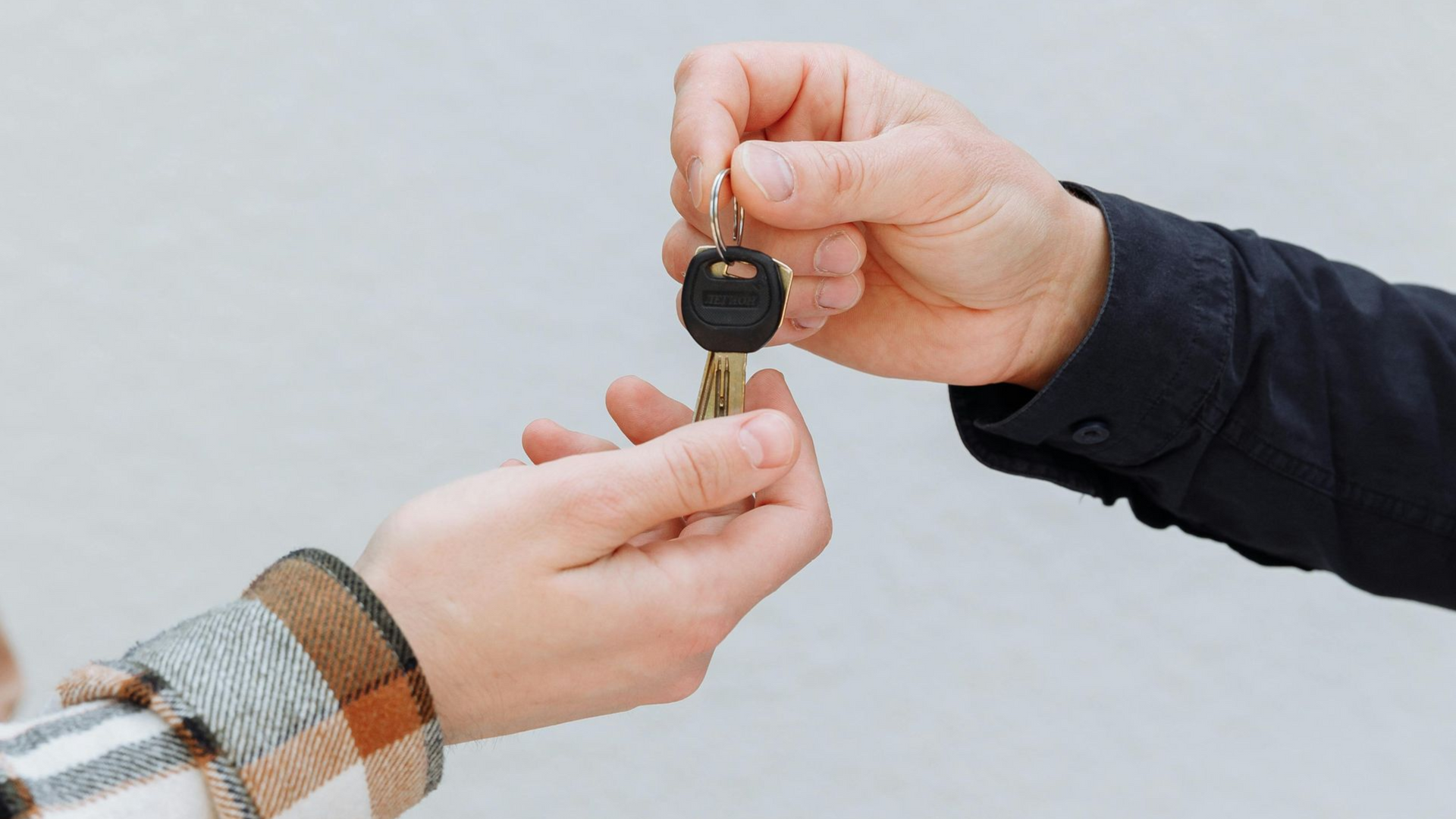 Hands passing keys against a light gray background; possibly a real estate transaction.