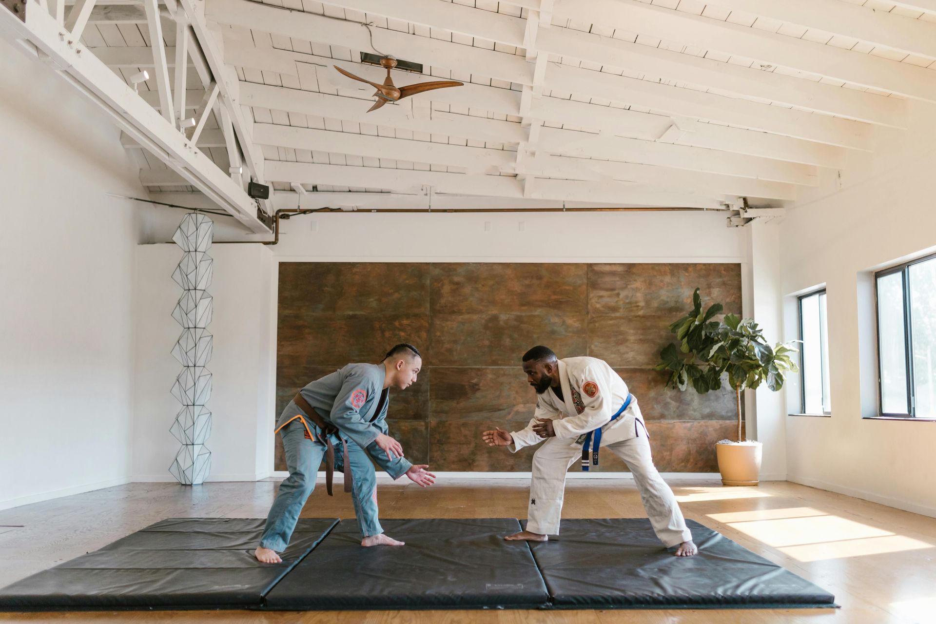 Two people in martial arts uniforms facing each other on a mat, indoors.