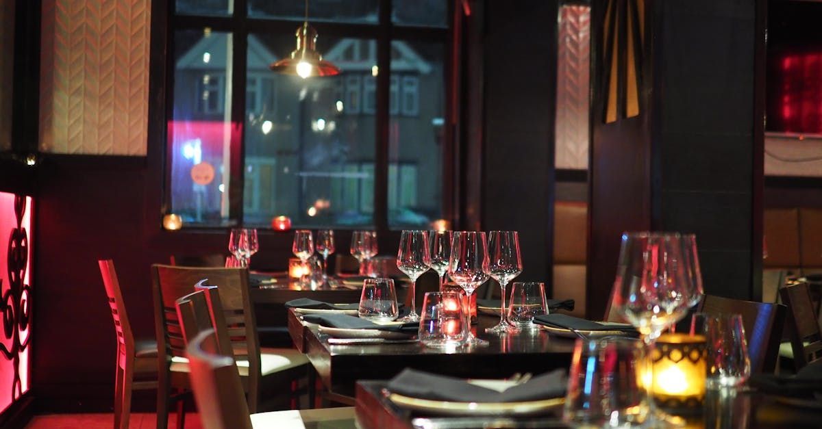 Upscale restaurant interior with set tables, lit candles, and a city view through the window at night.