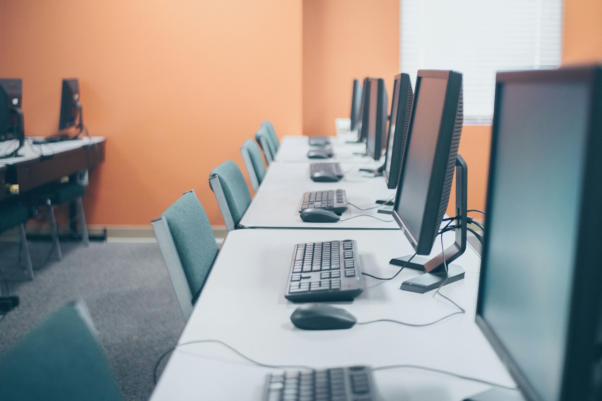Computer lab with rows of computers on white desks; orange wall.