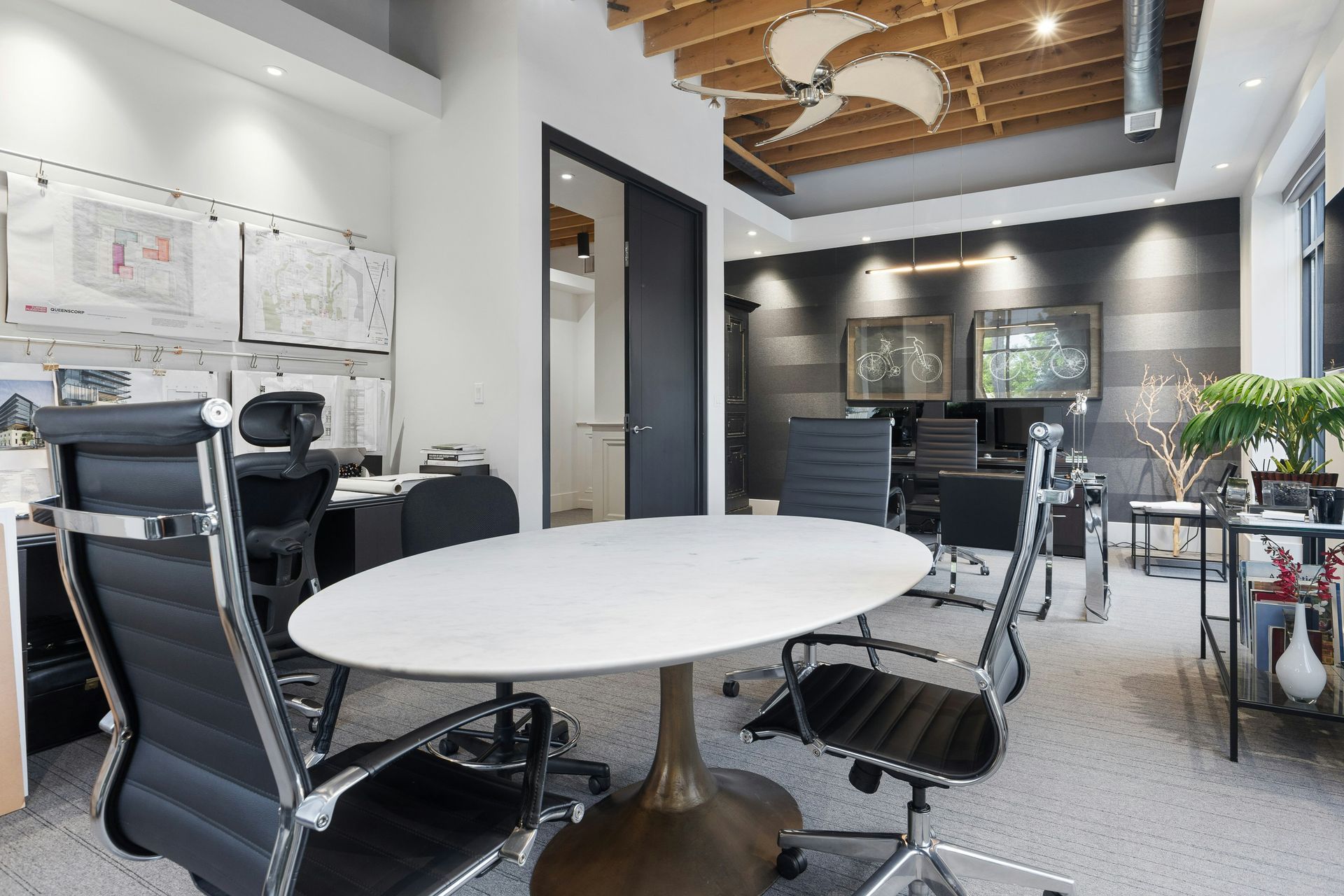 Office with round table, black chairs, drawings on wall, and exposed ceiling beams.