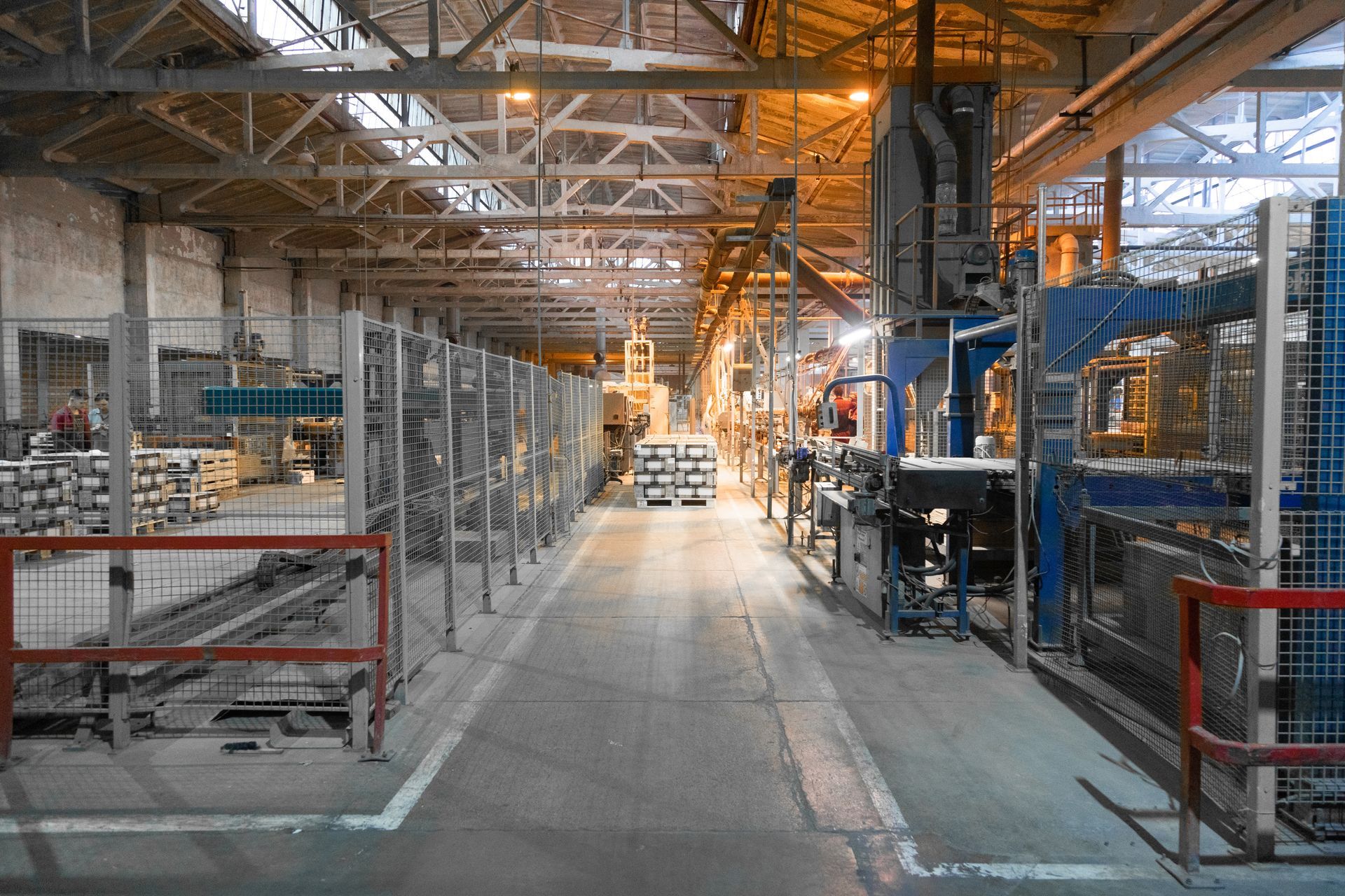 Inside a large factory, a long aisle with machinery and metal structures. Bright lighting.