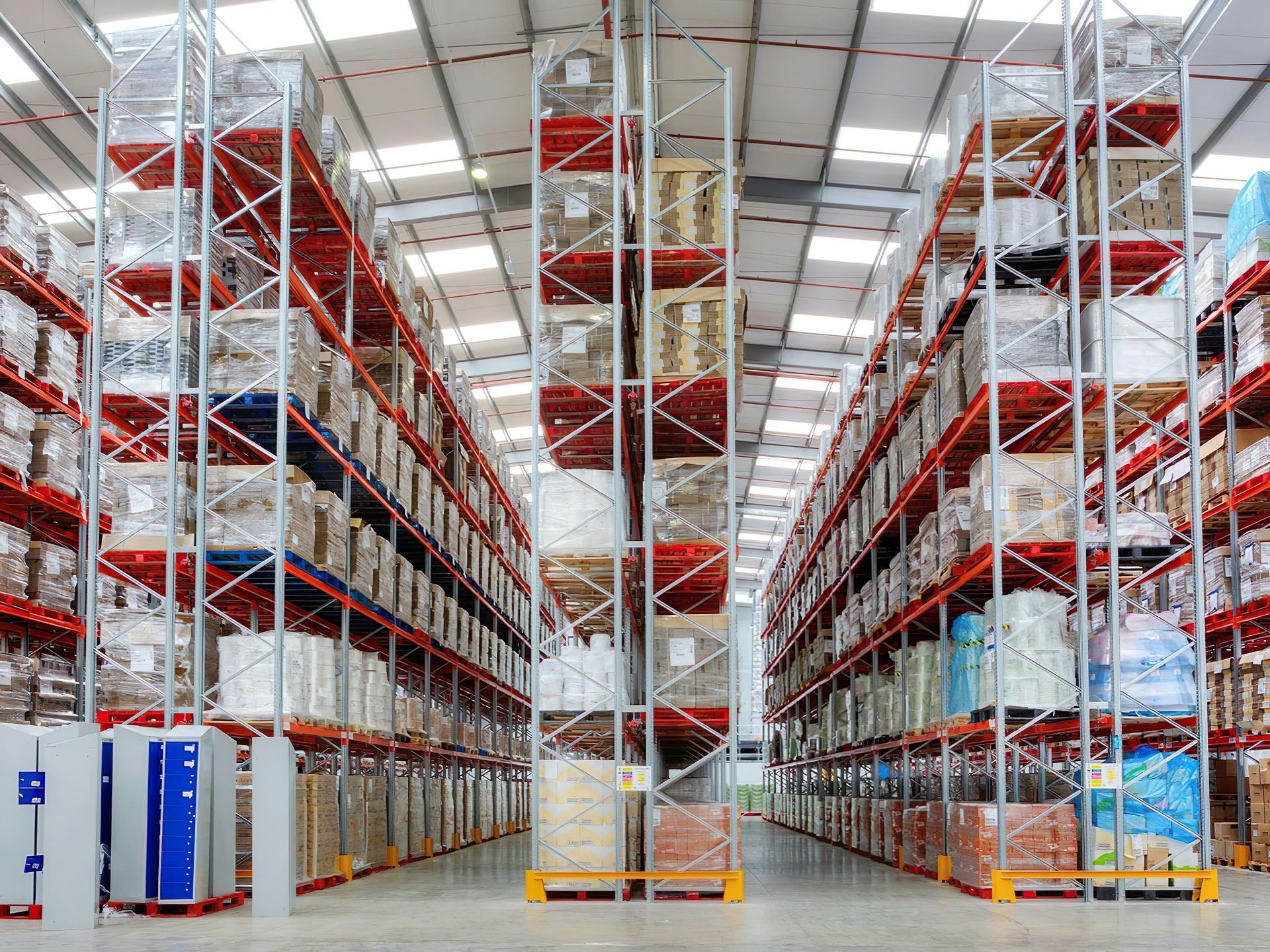 Rows of tall, packed shelving units inside a large warehouse. Goods are stored on multiple levels.