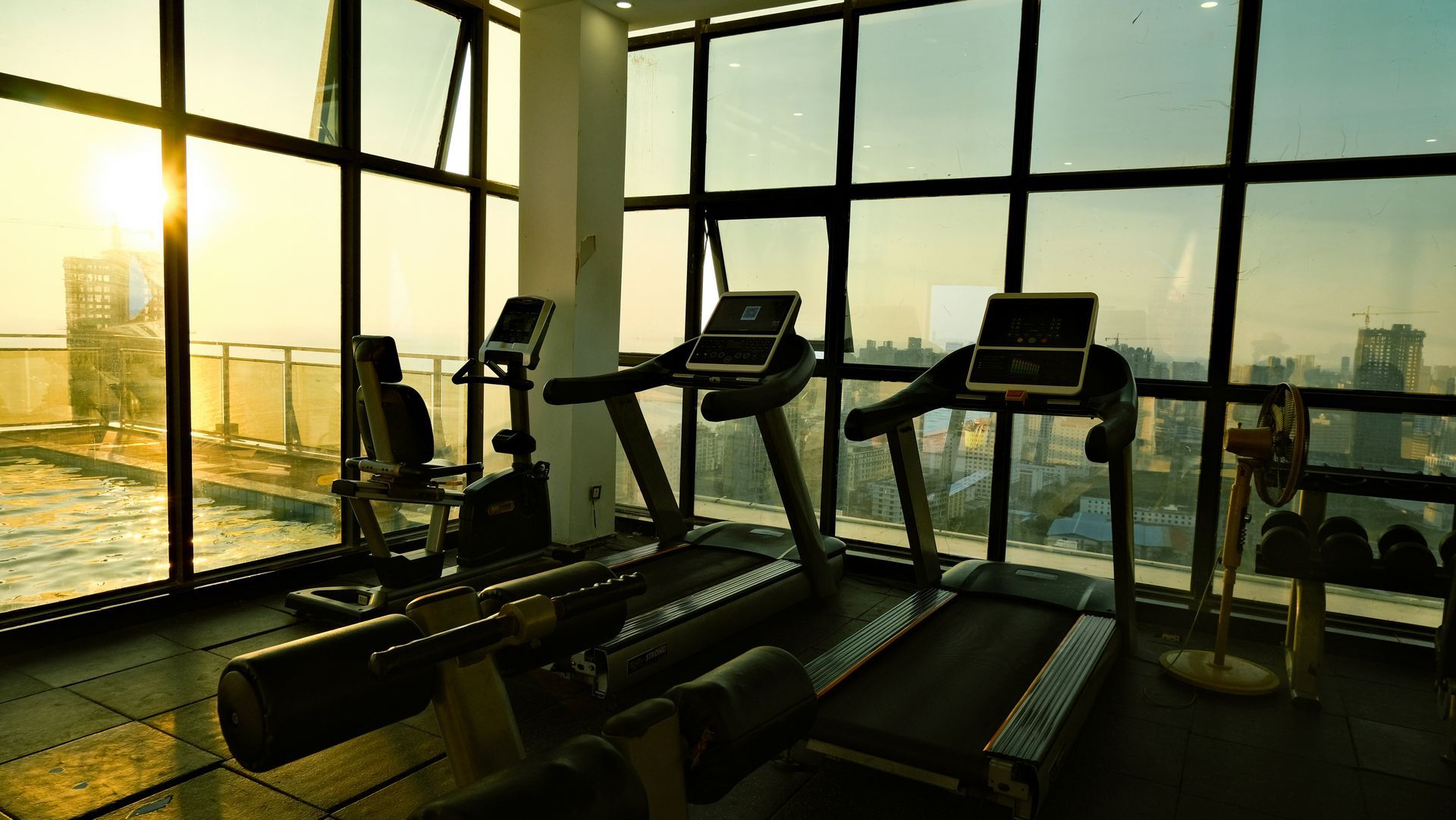 Gym with treadmills and exercise bike overlooking a city at sunrise.