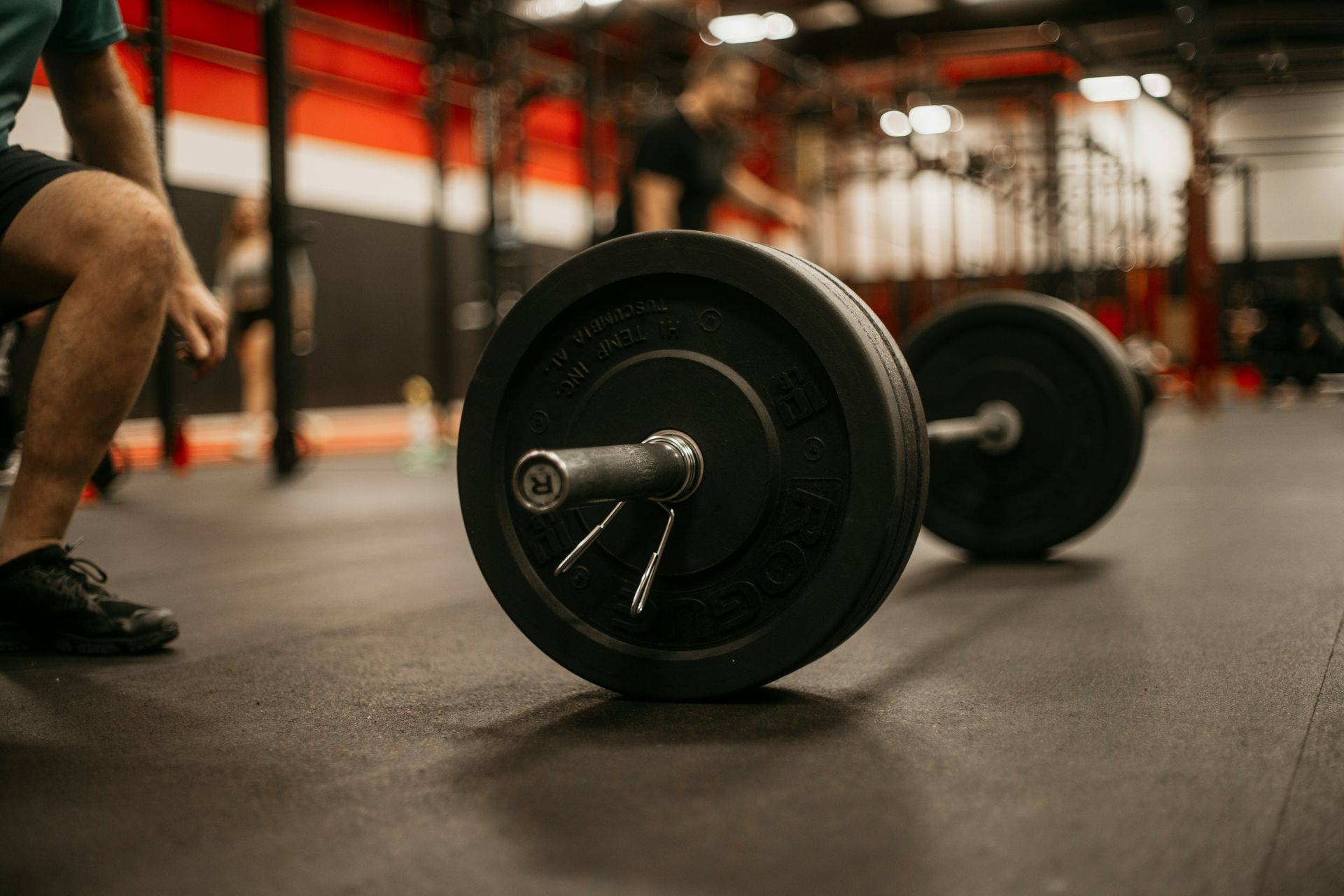 Barbell on gym floor with person in background.