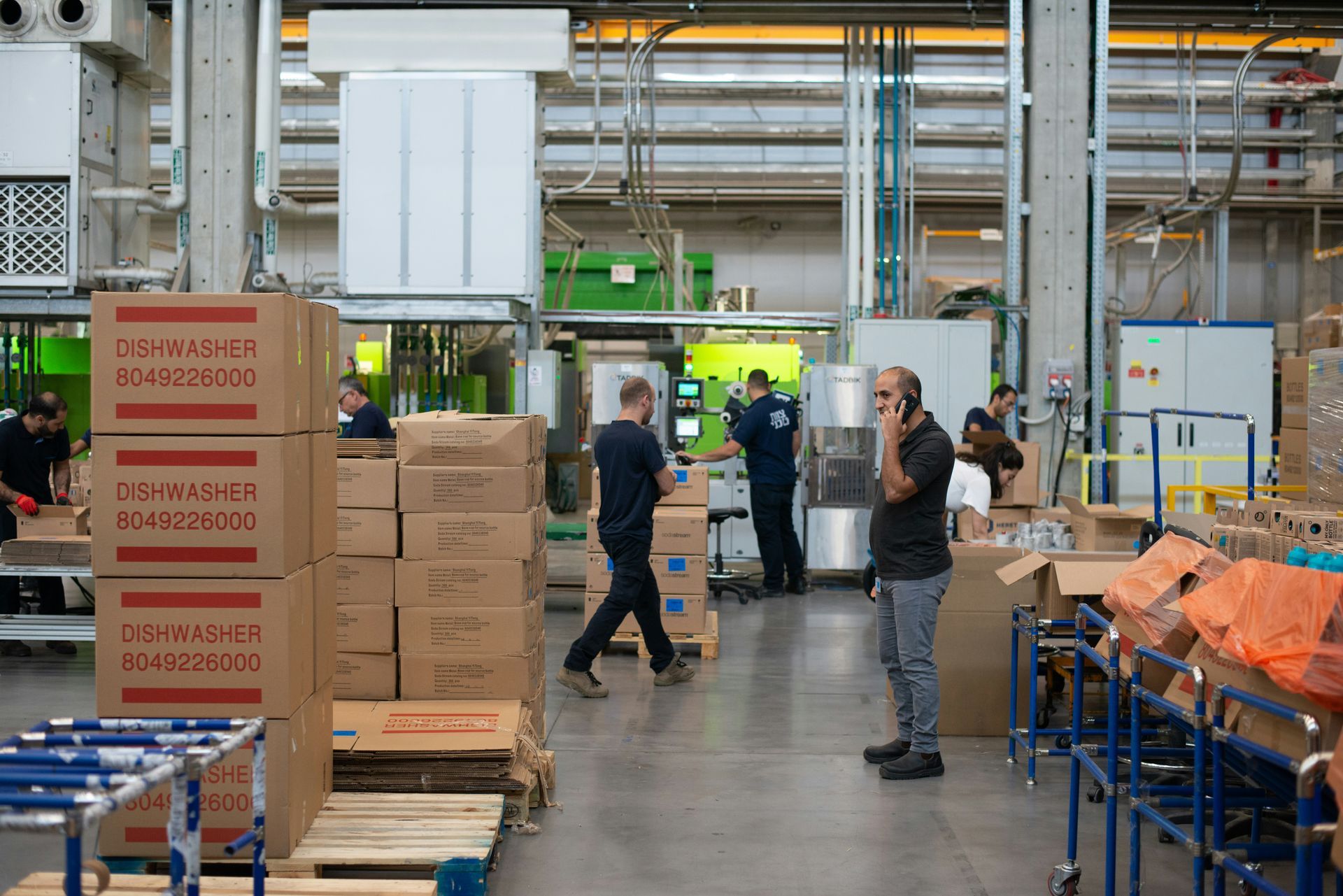 Warehouse interior with workers, boxes, and machinery. One man on phone.