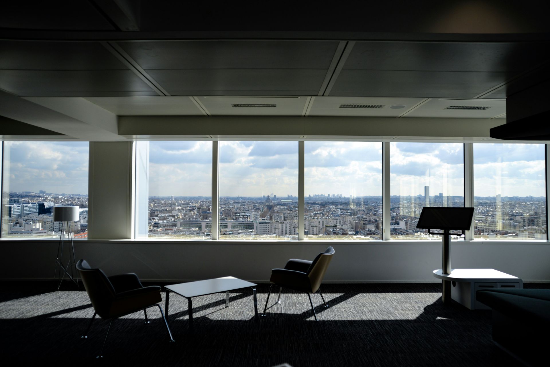 Interior view of a high-rise office with large windows overlooking a city, featuring two chairs, a table, and a stand.