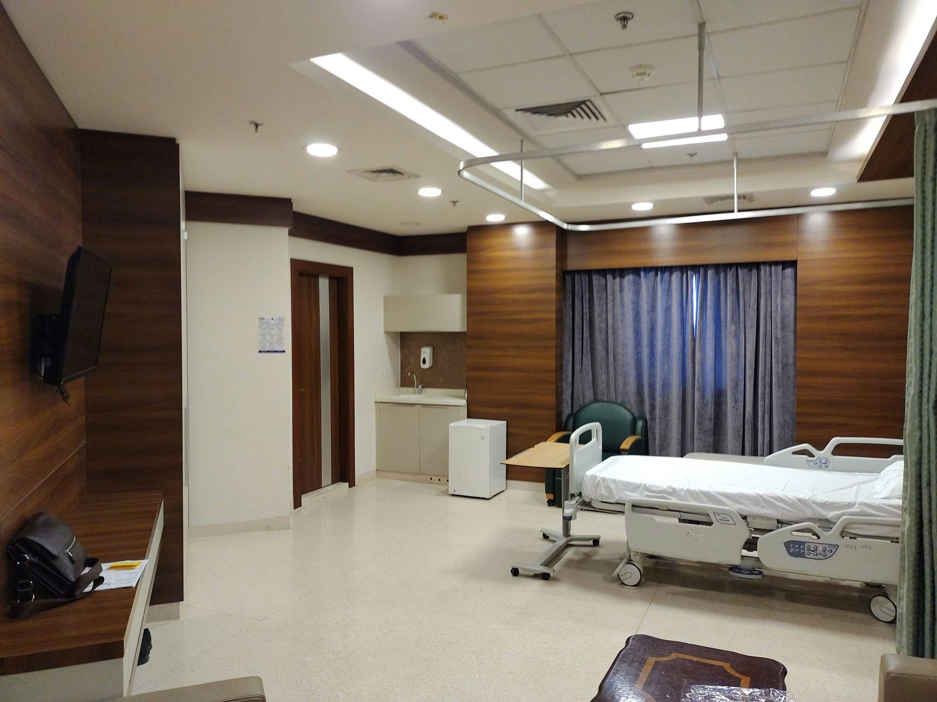 Hospital room with patient bed, wood paneling, and a window with curtains.