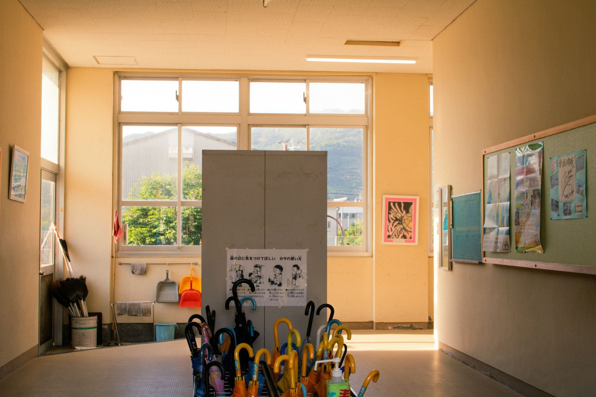 School hallway with sunlight, windows, umbrellas, and artwork.