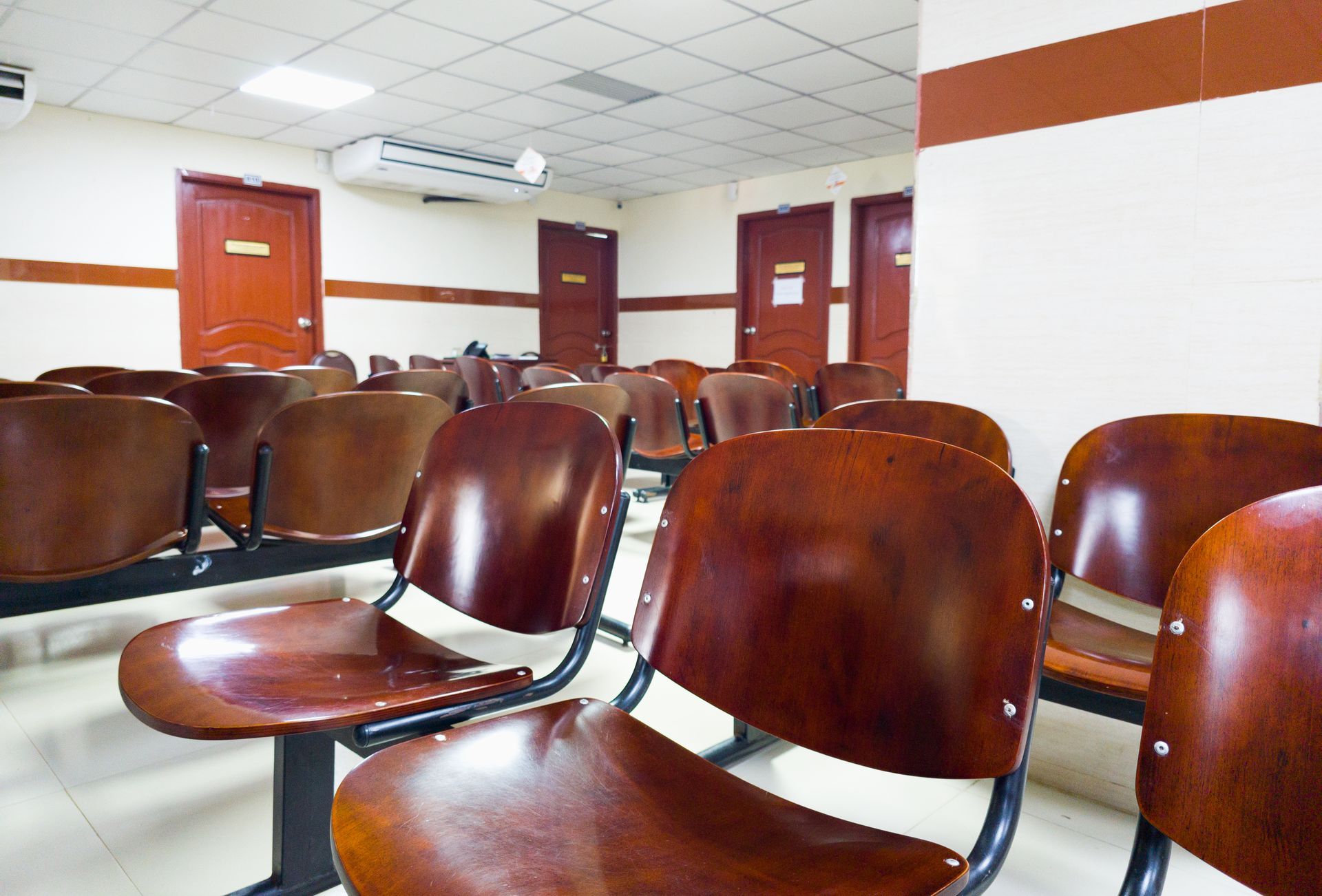 Waiting room with rows of wood chairs facing brown doors.