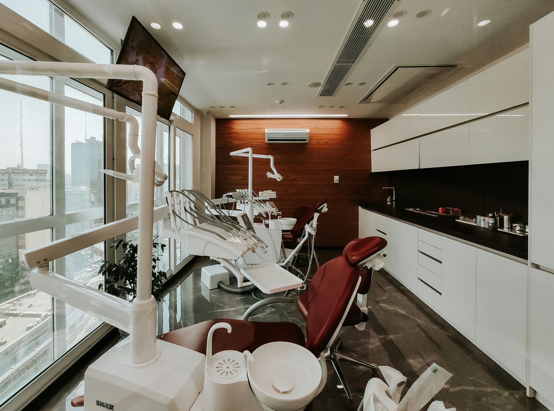 Modern dental office with a chair, tools, cabinetry, and a large window with a city view.