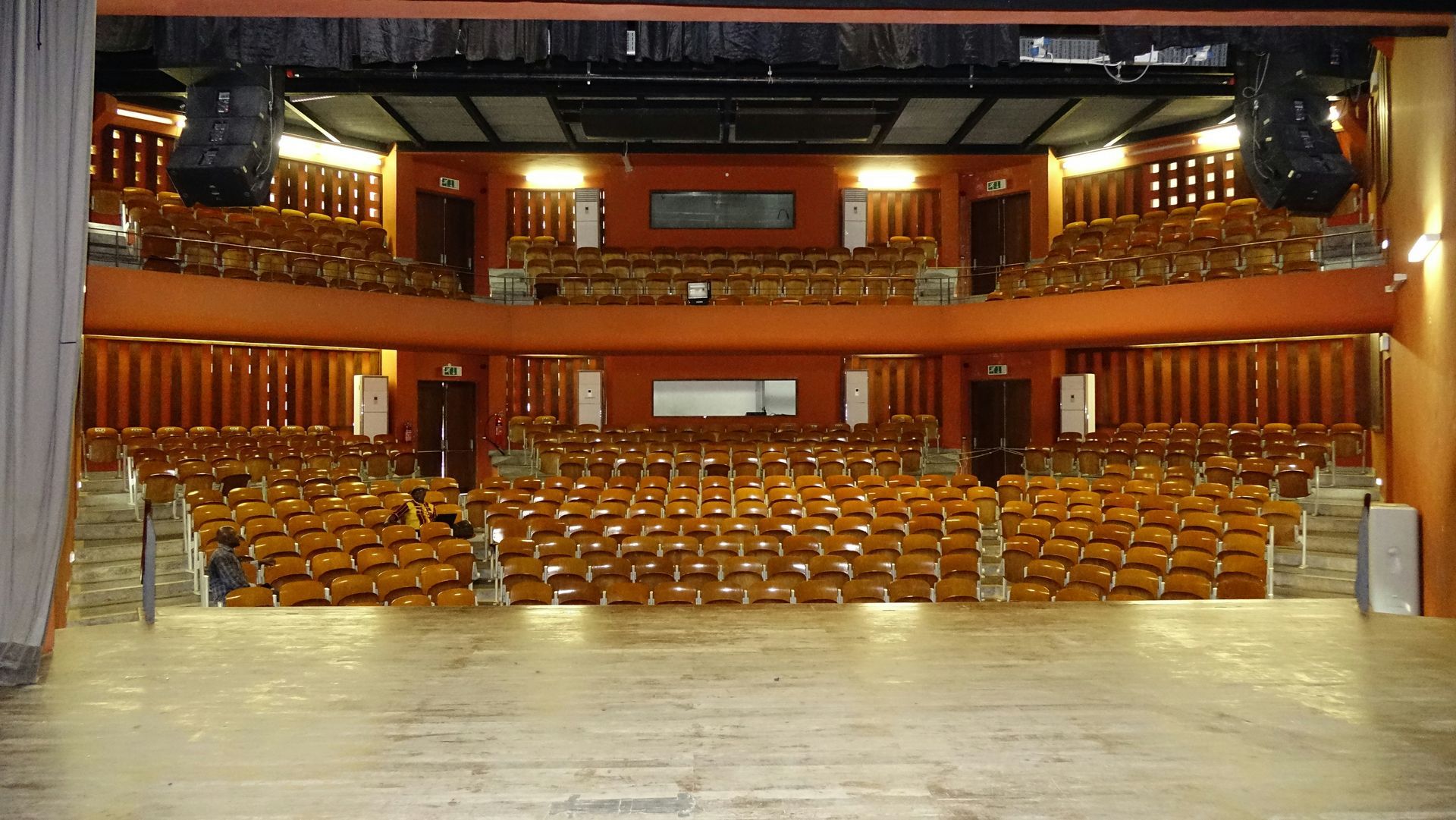 Empty theater auditorium with tiered seating, brown chairs, and stage.