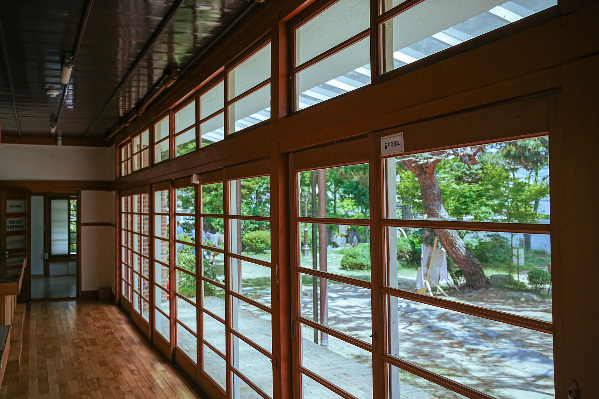 Wooden-framed windows line a room overlooking a garden. Bright light fills the space.
