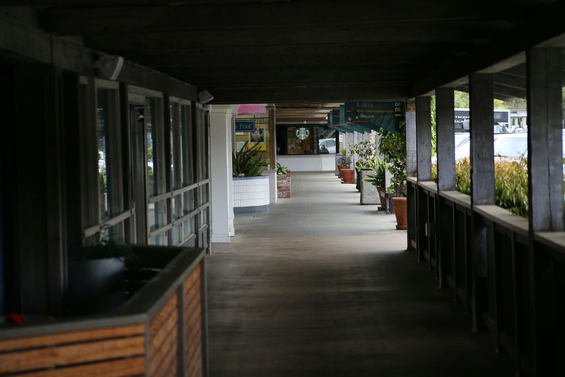 Covered walkway lined with shops. Starbucks visible in the distance. Wooden beams overhead.