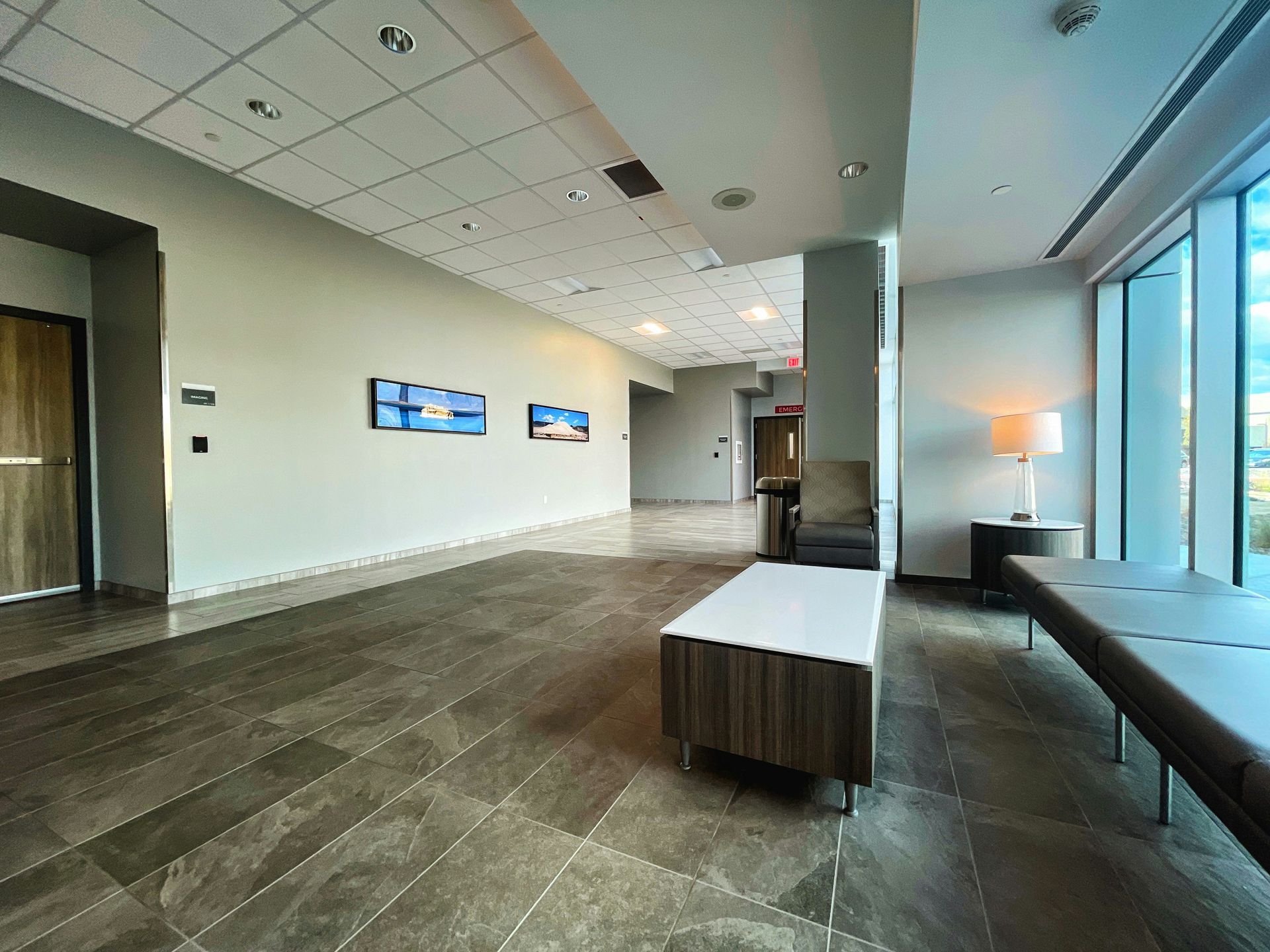 Hallway with tiled floor, benches, artwork, and large windows.