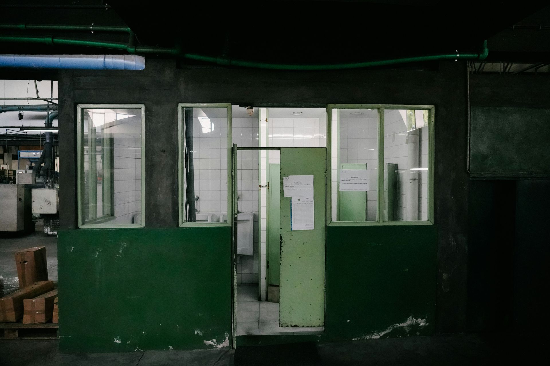 Green-painted industrial control booth with windows and open doorway; dark setting, possibly a factory.