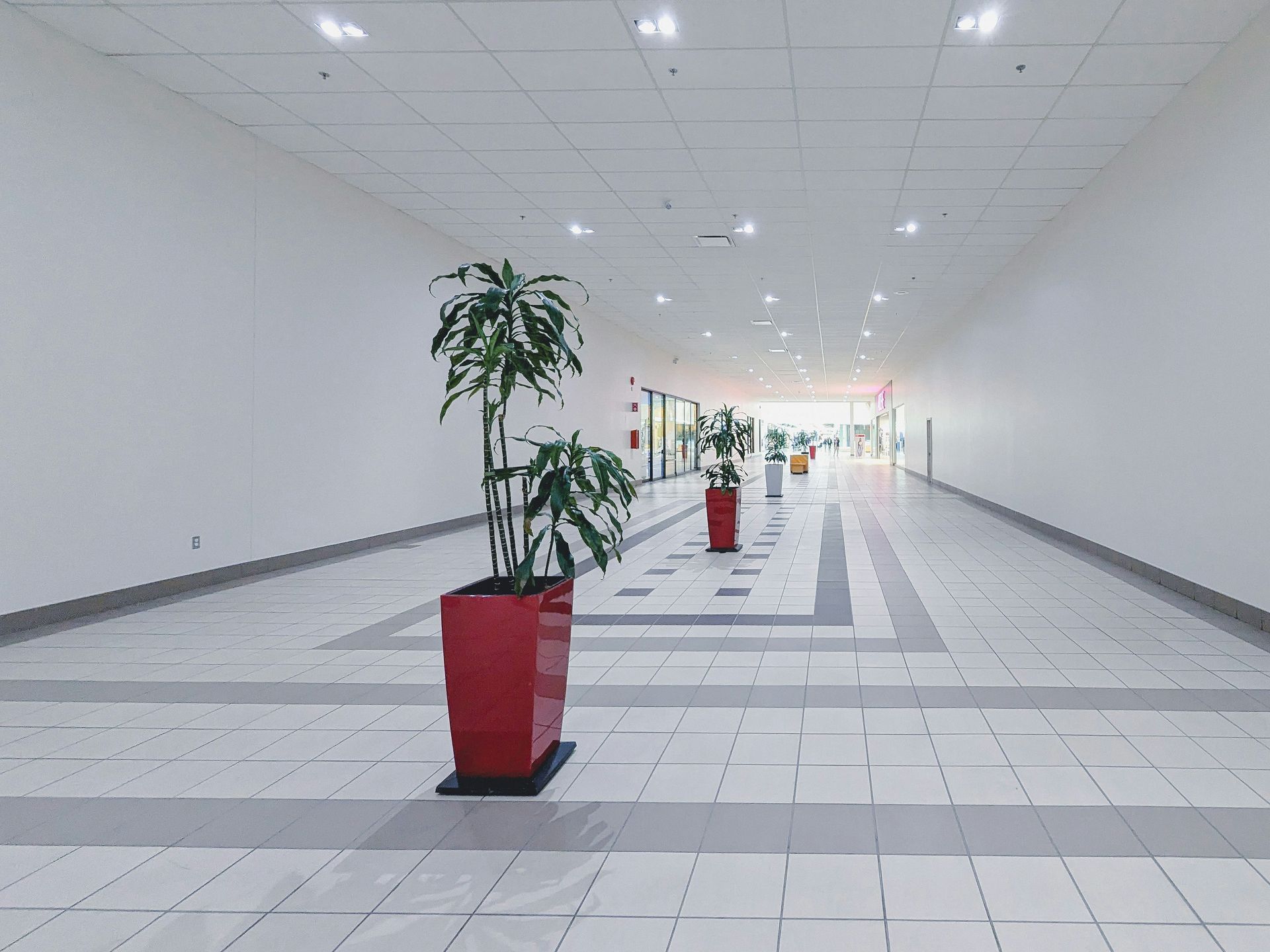 Empty mall hallway with white walls and red planters.