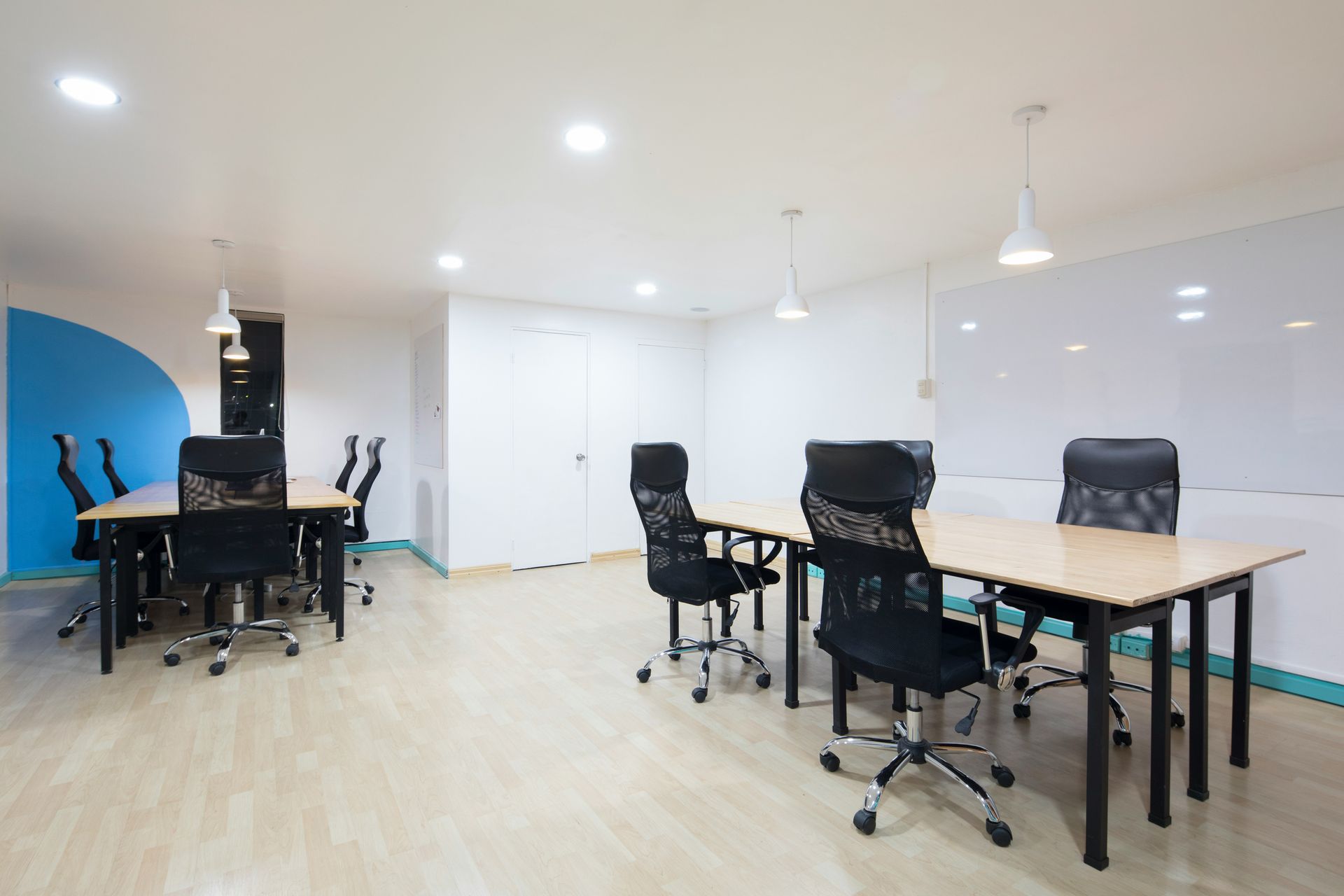 Empty office space with desks and chairs, white walls, and wood flooring.