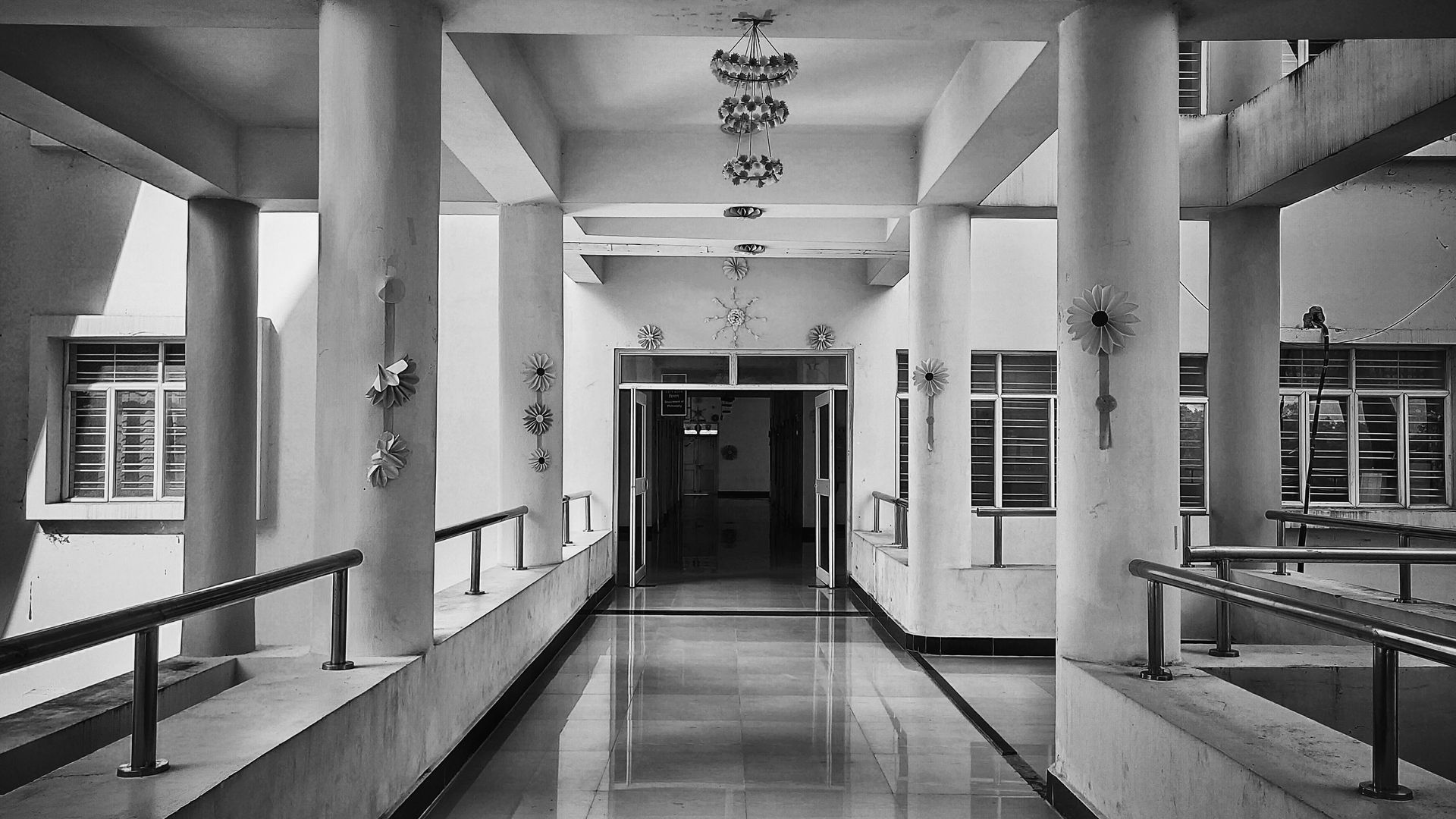 Hallway with white pillars, windows, and railings, leading to an open doorway at the end.
