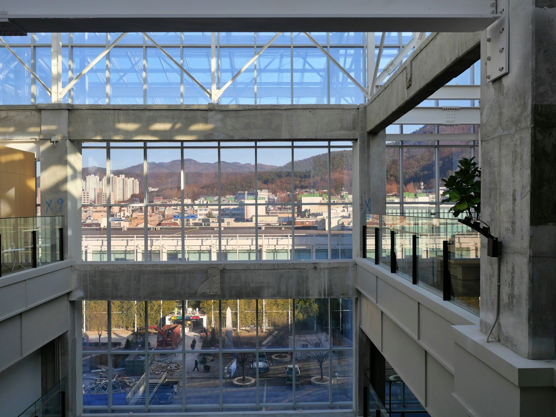 Interior view of a modern building with large windows overlooking a city and mountains under a blue sky.