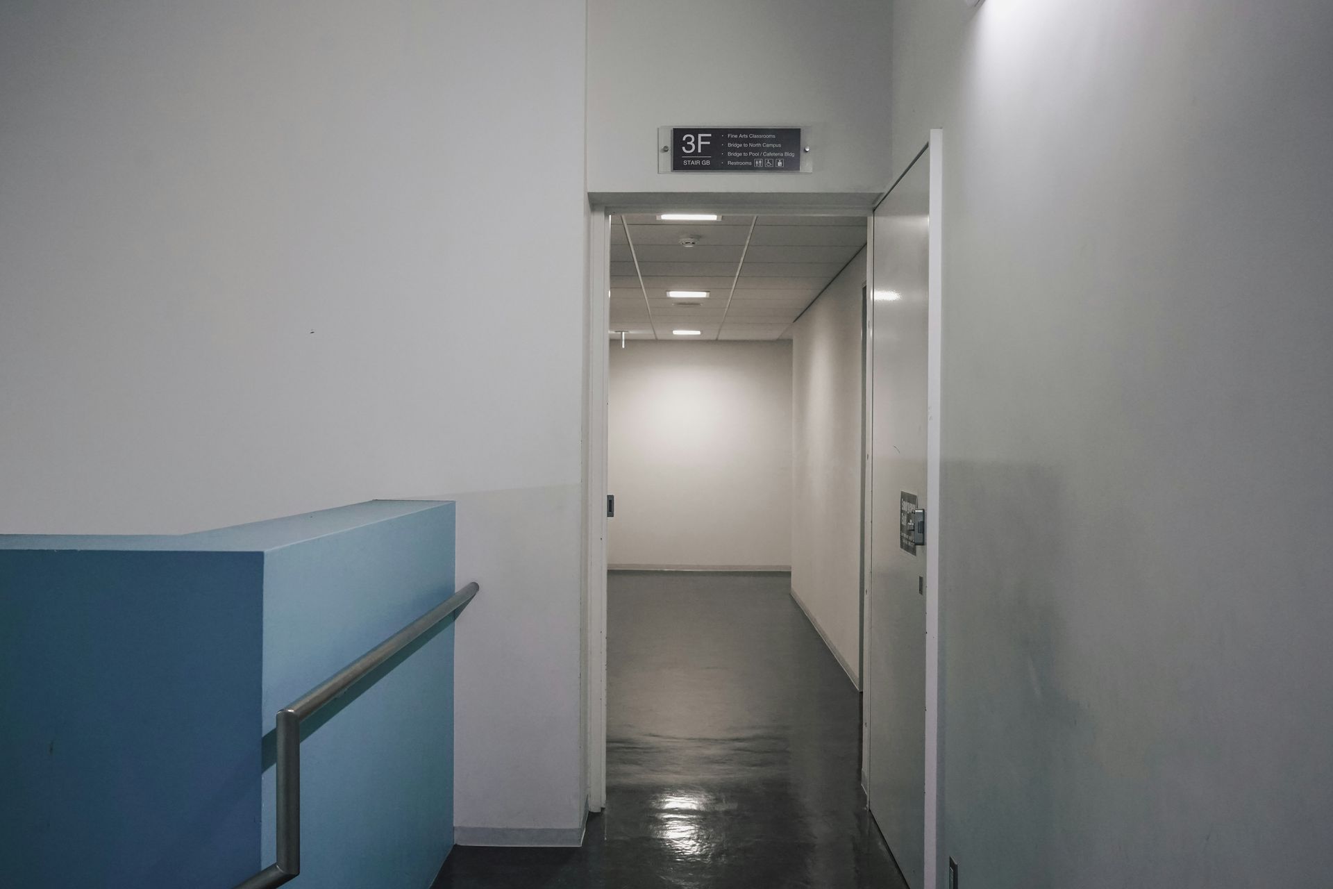 Hallway with white walls, gray floor, open door, and a blue structure with a handrail.