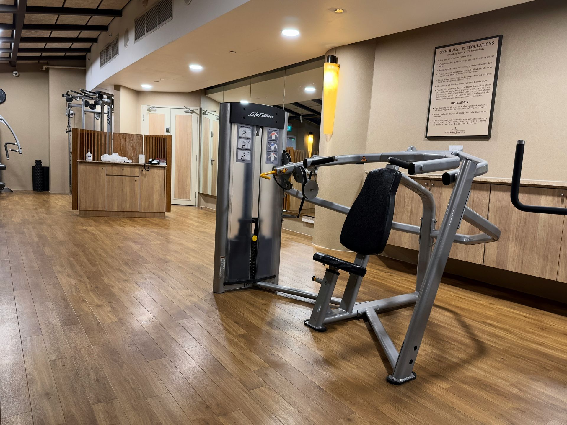 Gym interior with a chest press machine on a wood floor.