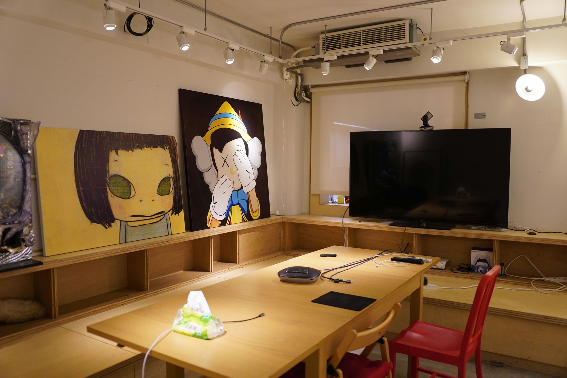 Meeting room with art on the walls, large TV, table with lamp and tech, red chair.