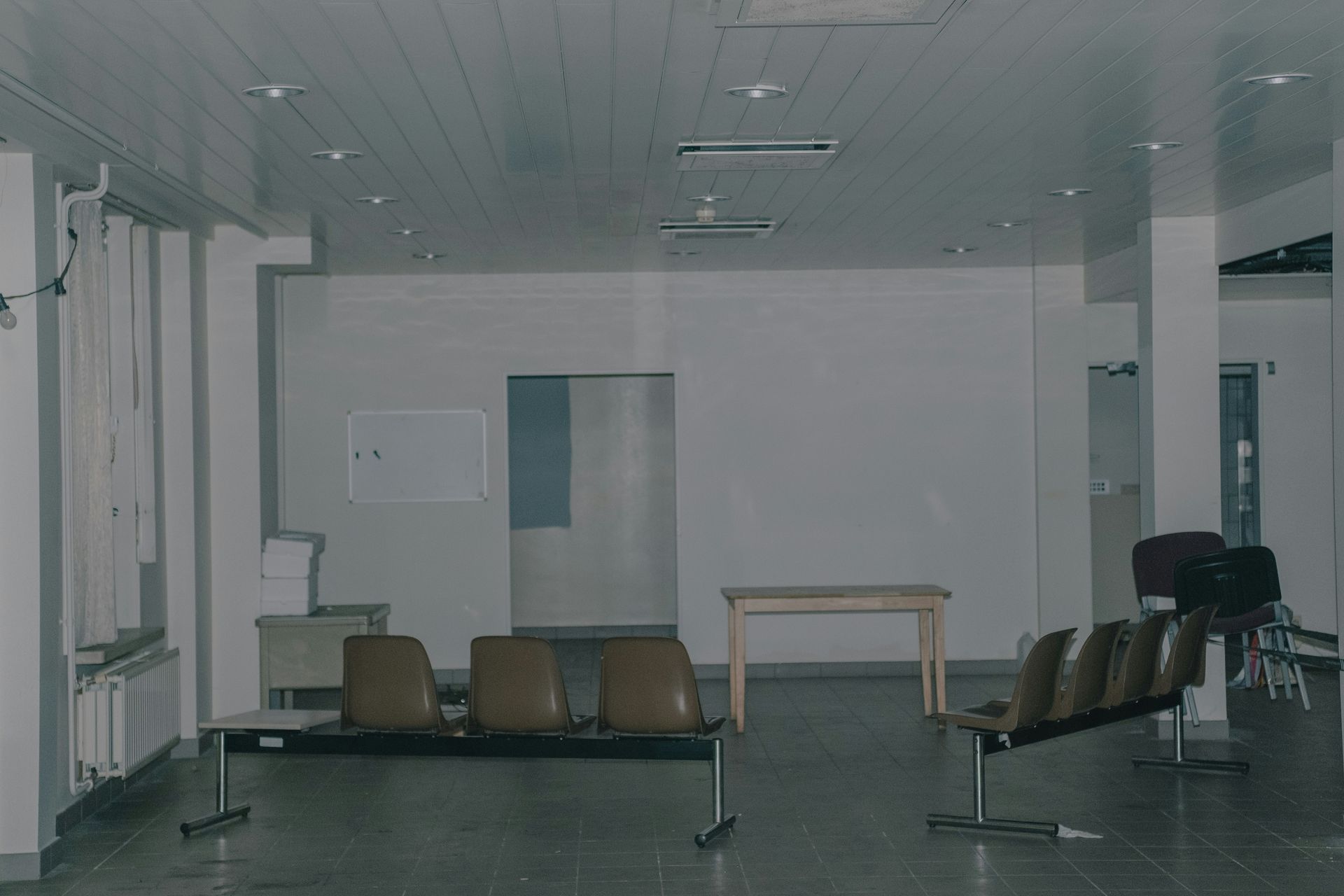 Waiting room with several brown benches, white walls, and a wooden table.