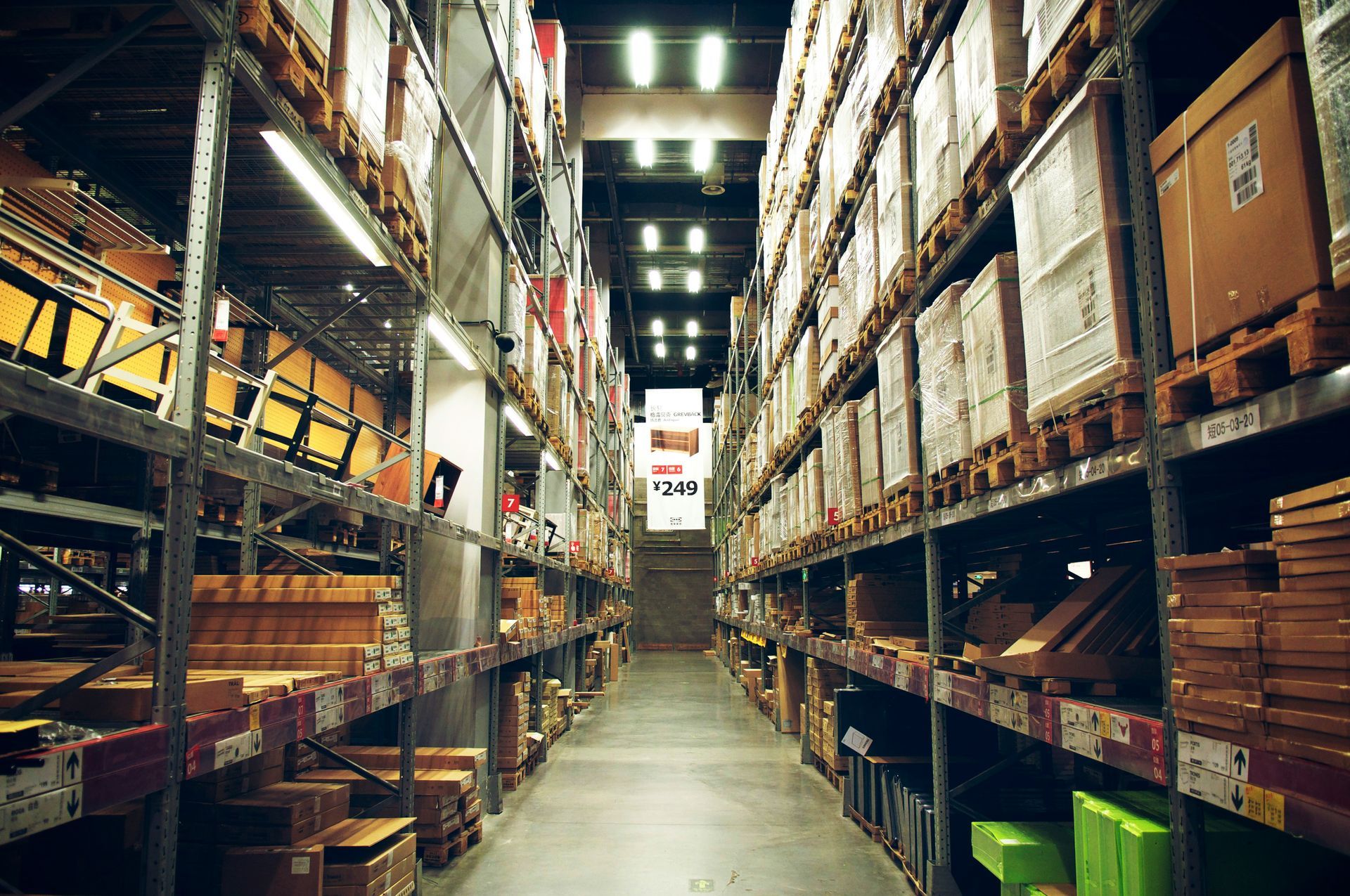 Warehouse interior with shelves stacked with boxes, lit by overhead lights.