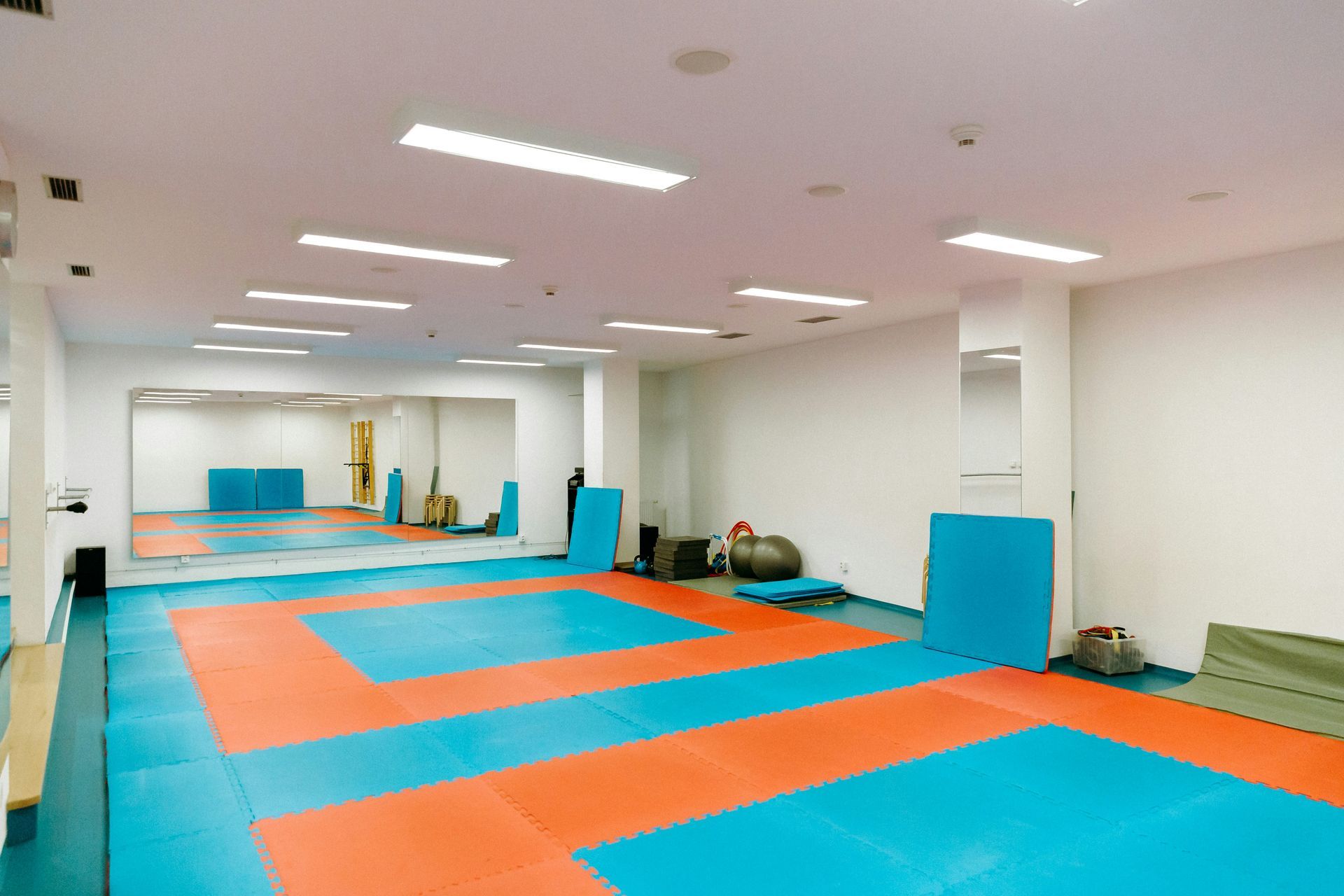 Gym interior with blue and orange mats, mirrors, and training equipment.