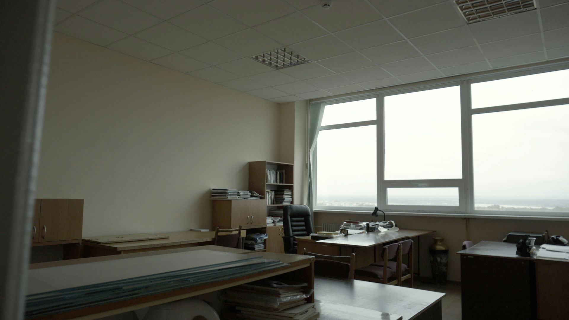 Empty office with a large window. Desks, bookshelves, and various office supplies are visible.