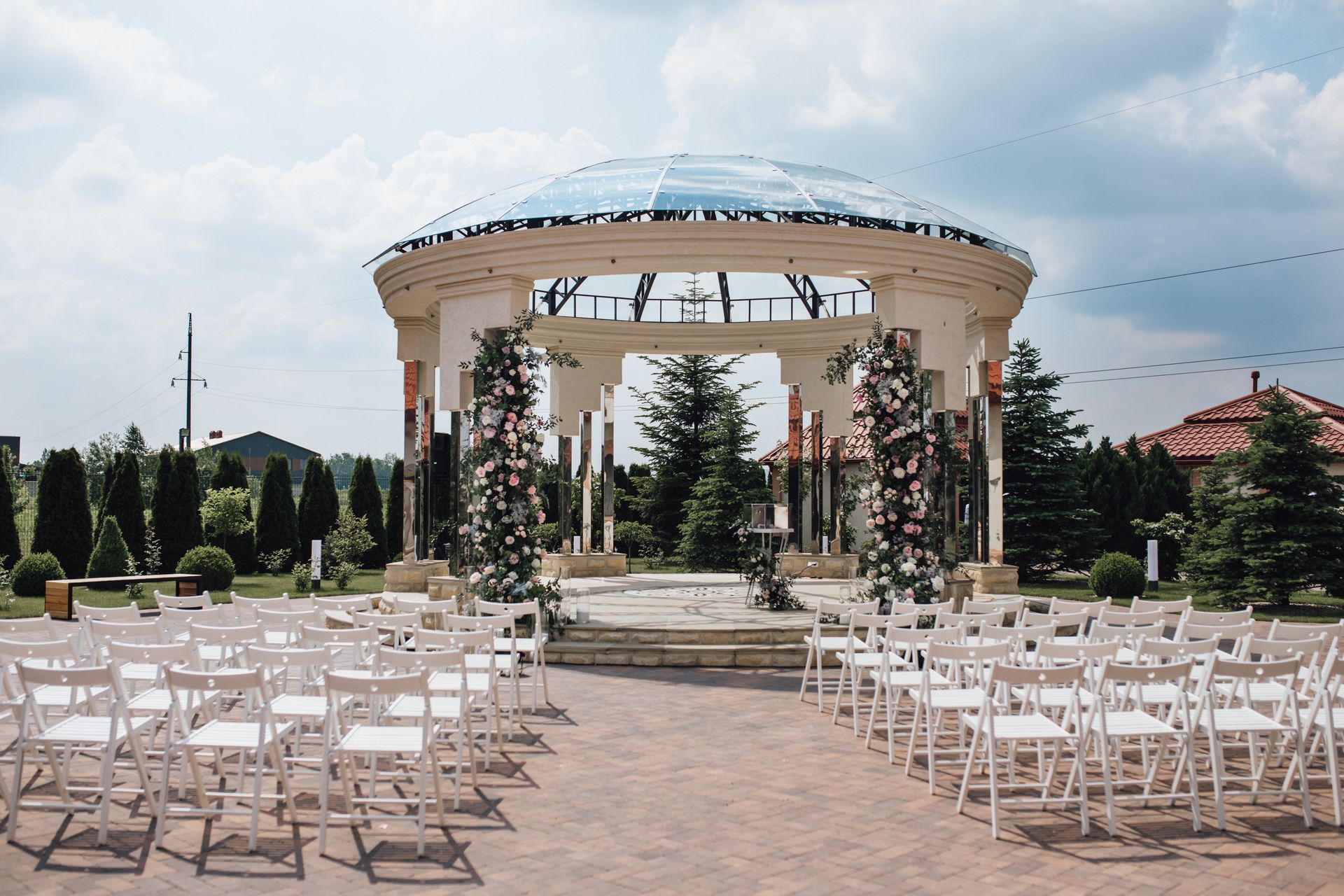 Wedding ceremony setup with white chairs, brick pathway, and a decorative gazebo.