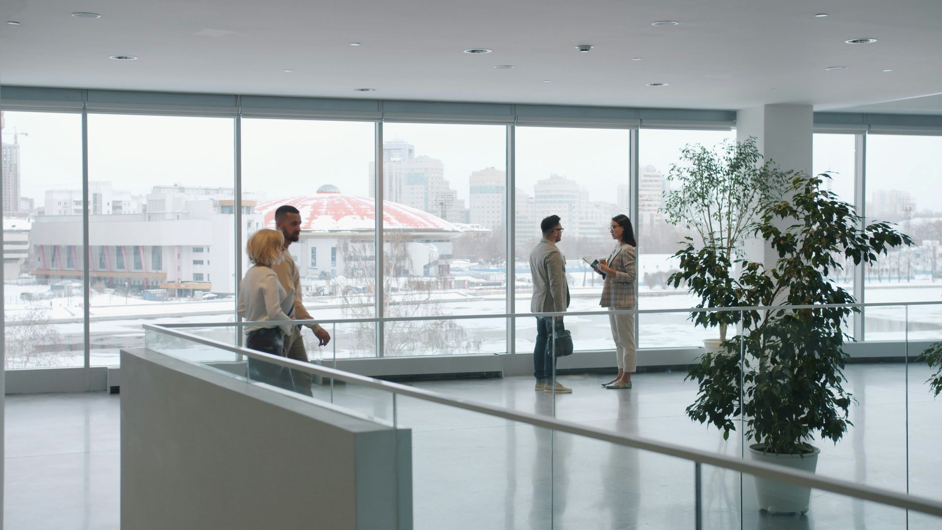 People in an office atrium with large windows overlooking a city.