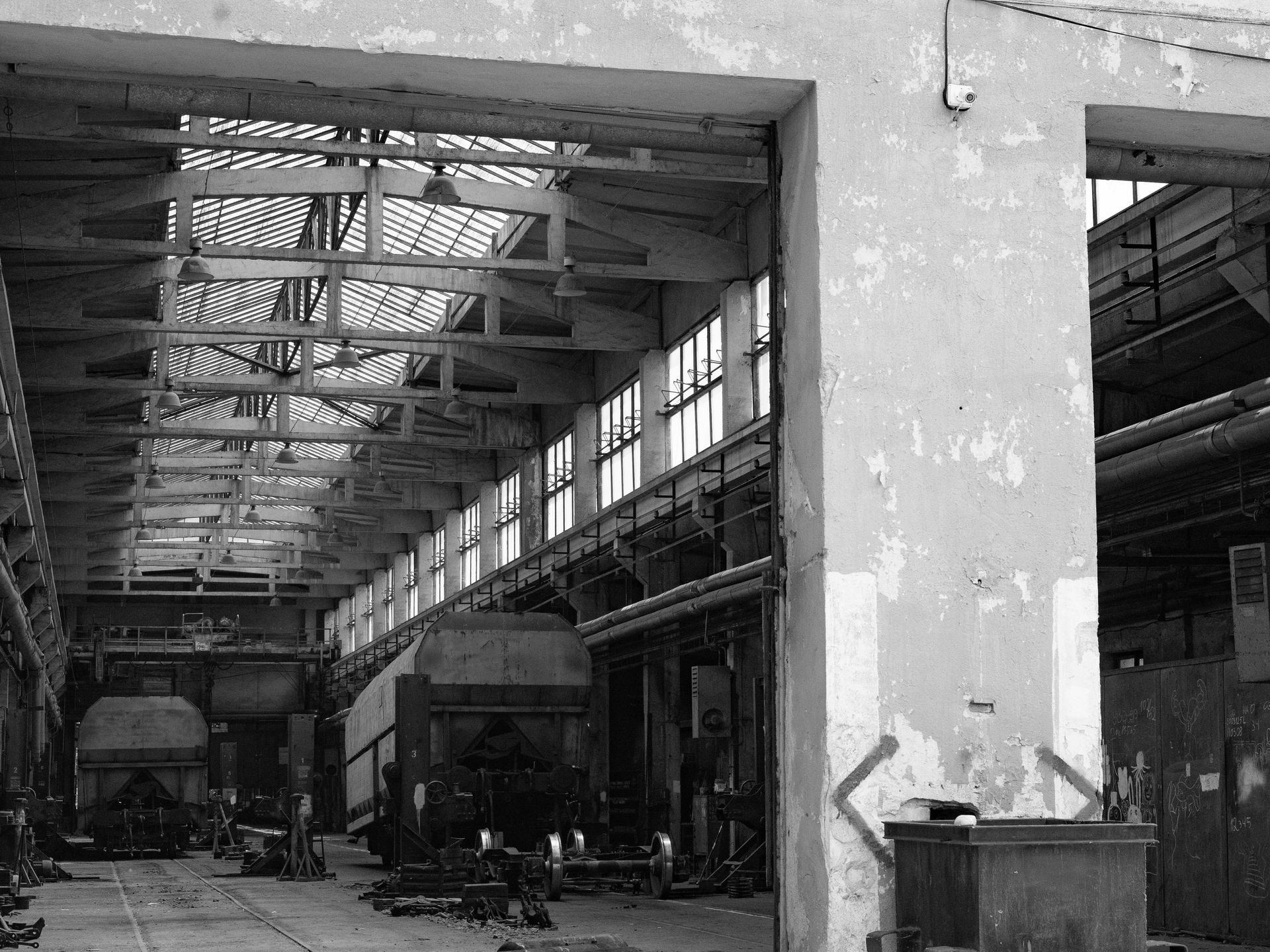 Inside a large, weathered industrial building; rail cars are lined up on tracks.