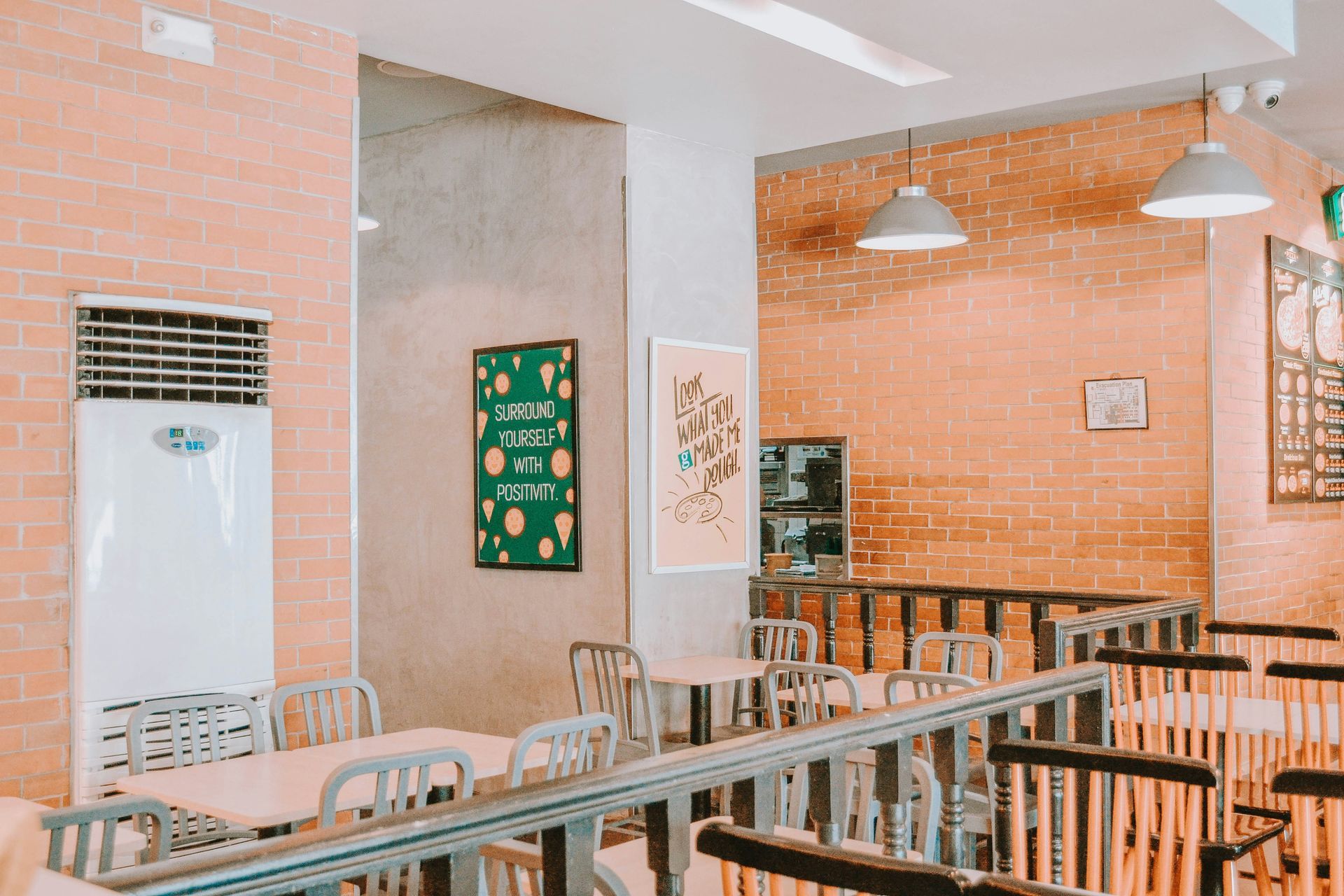 Restaurant interior with brick walls, tables, chairs, and hanging lights.