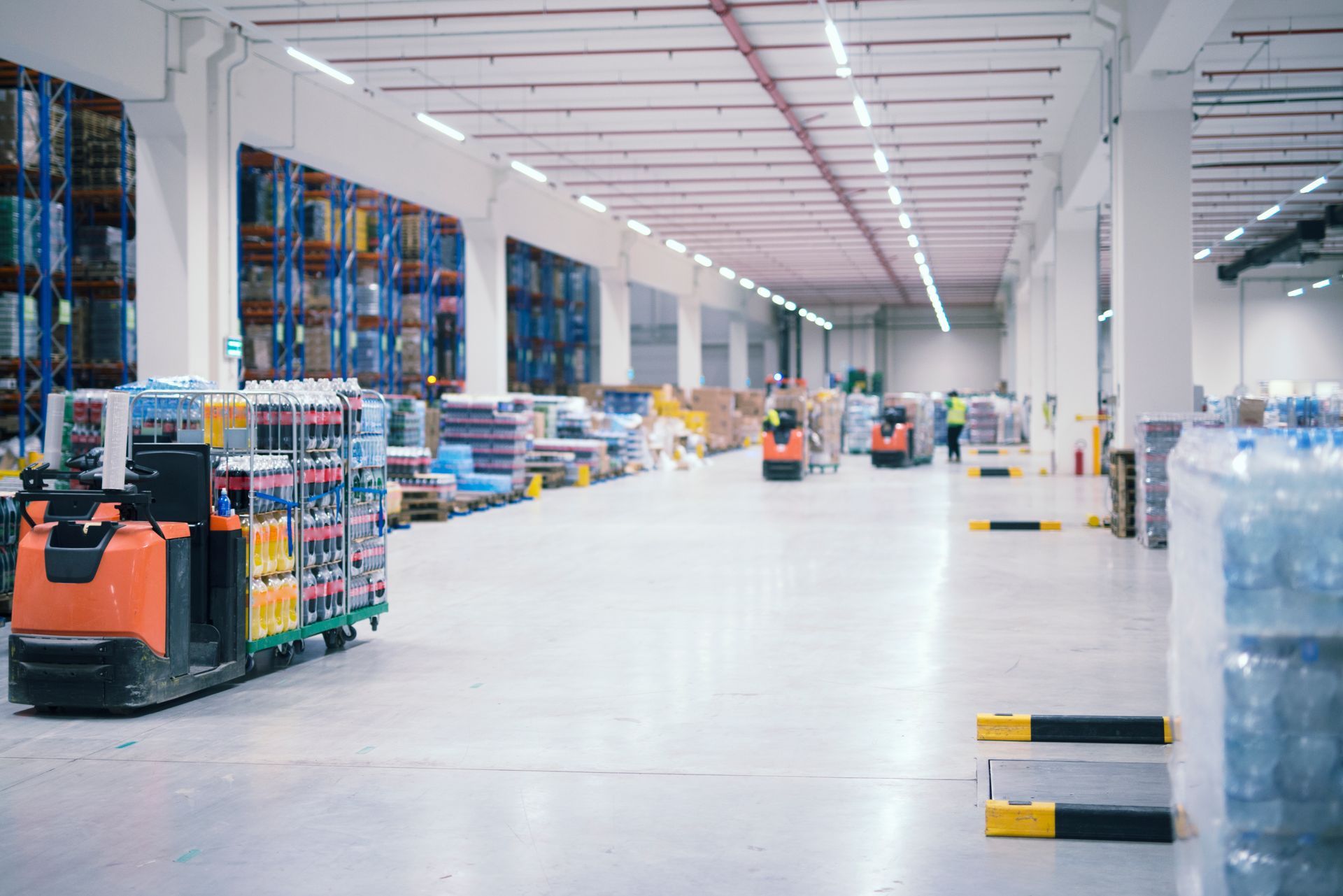 Warehouse interior with forklifts and stacked goods.