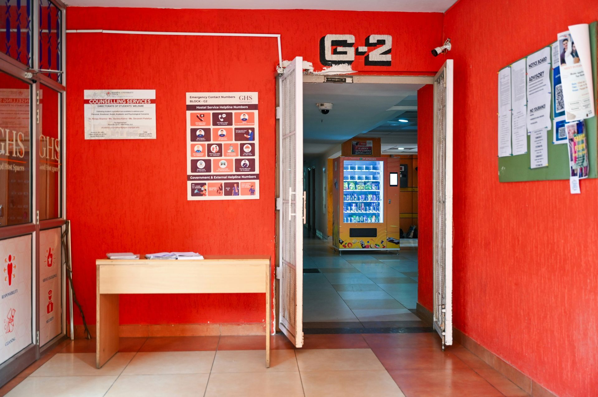 Entrance to G-2 with open doors, red walls, vending machine visible, and a small desk.