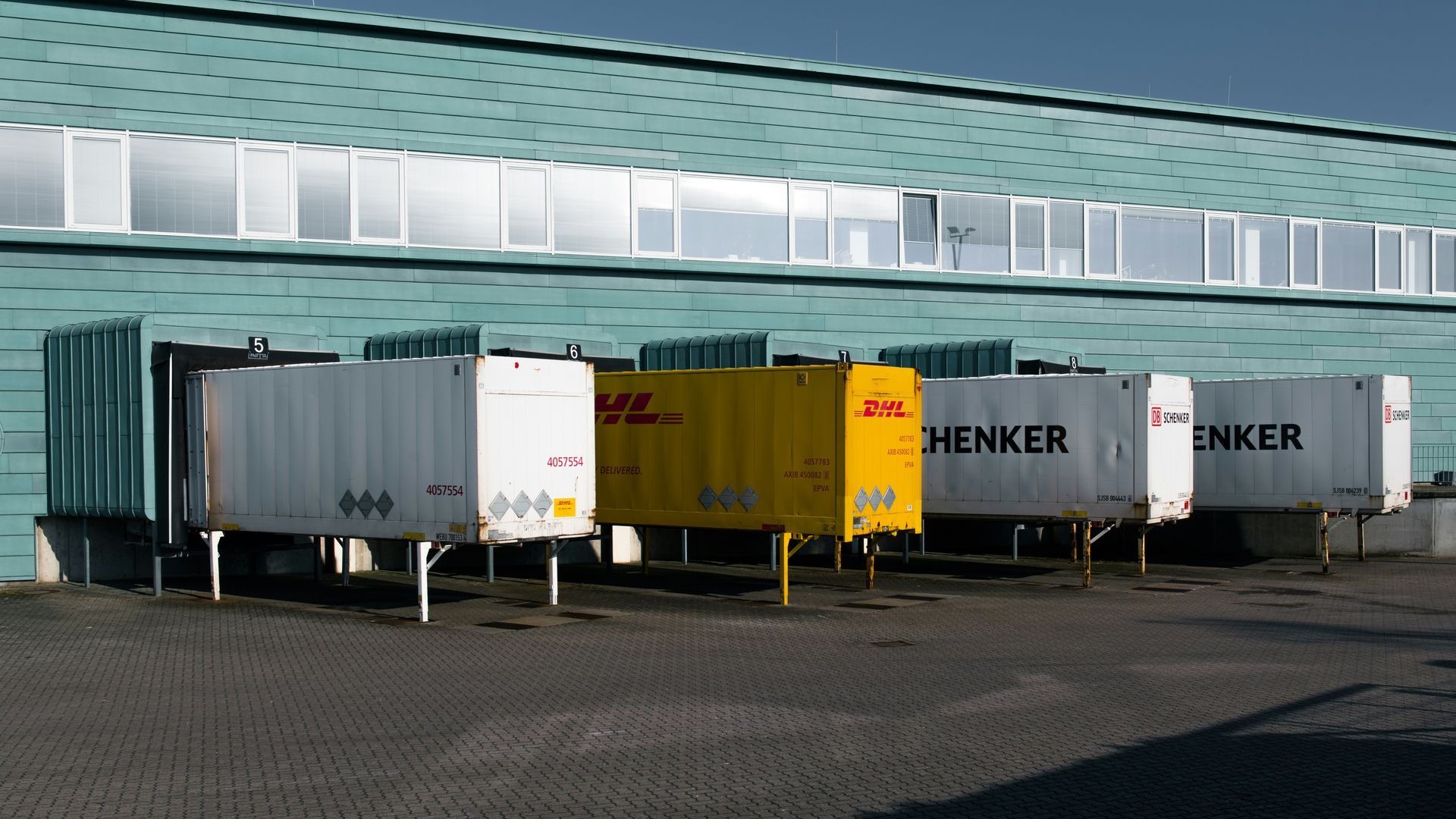 Shipping containers at a loading dock with DHL and Schenker branding.