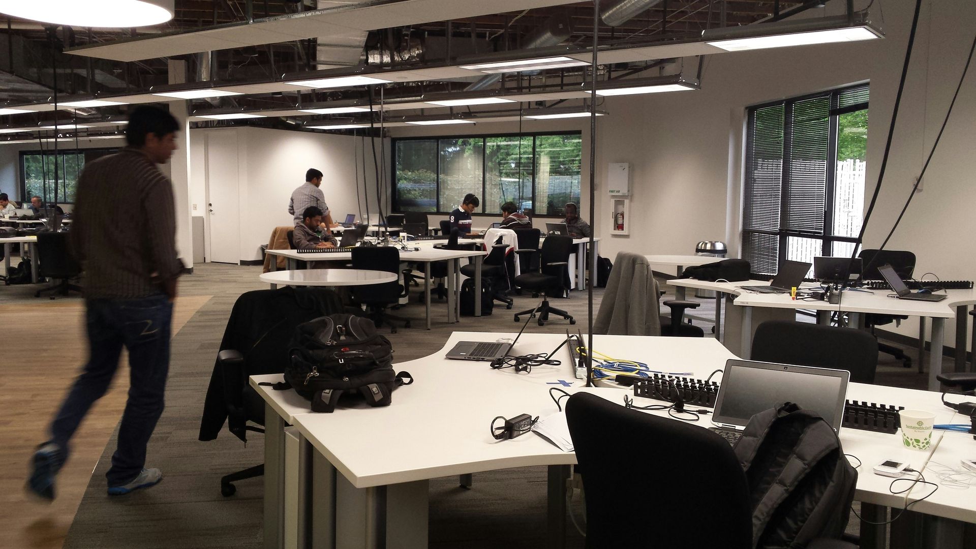 Man walks through a modern office. Desks with computers, people working, natural light.