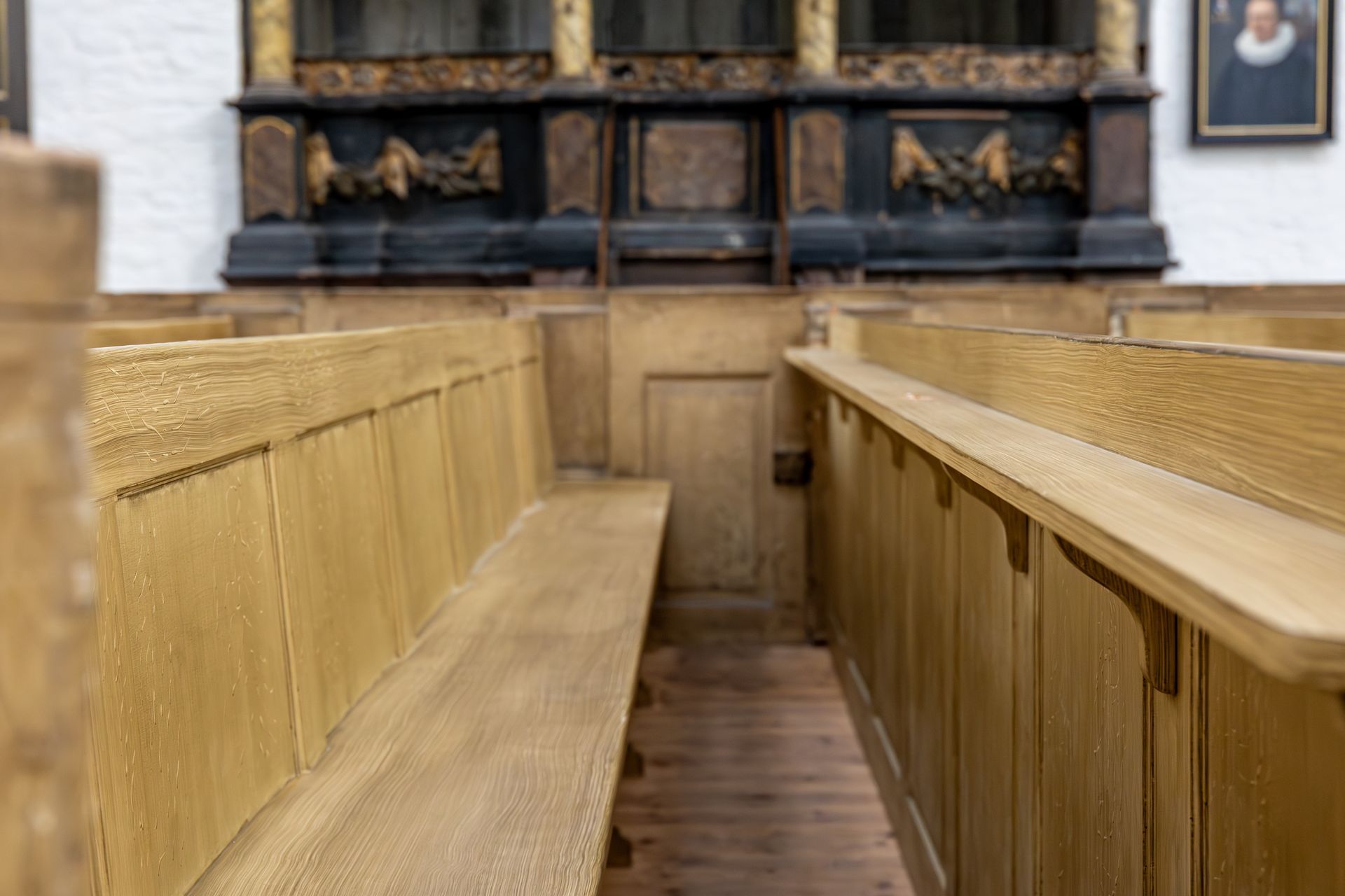 Wooden church pews with a decorated altar in the background. Light wood tones dominate.
