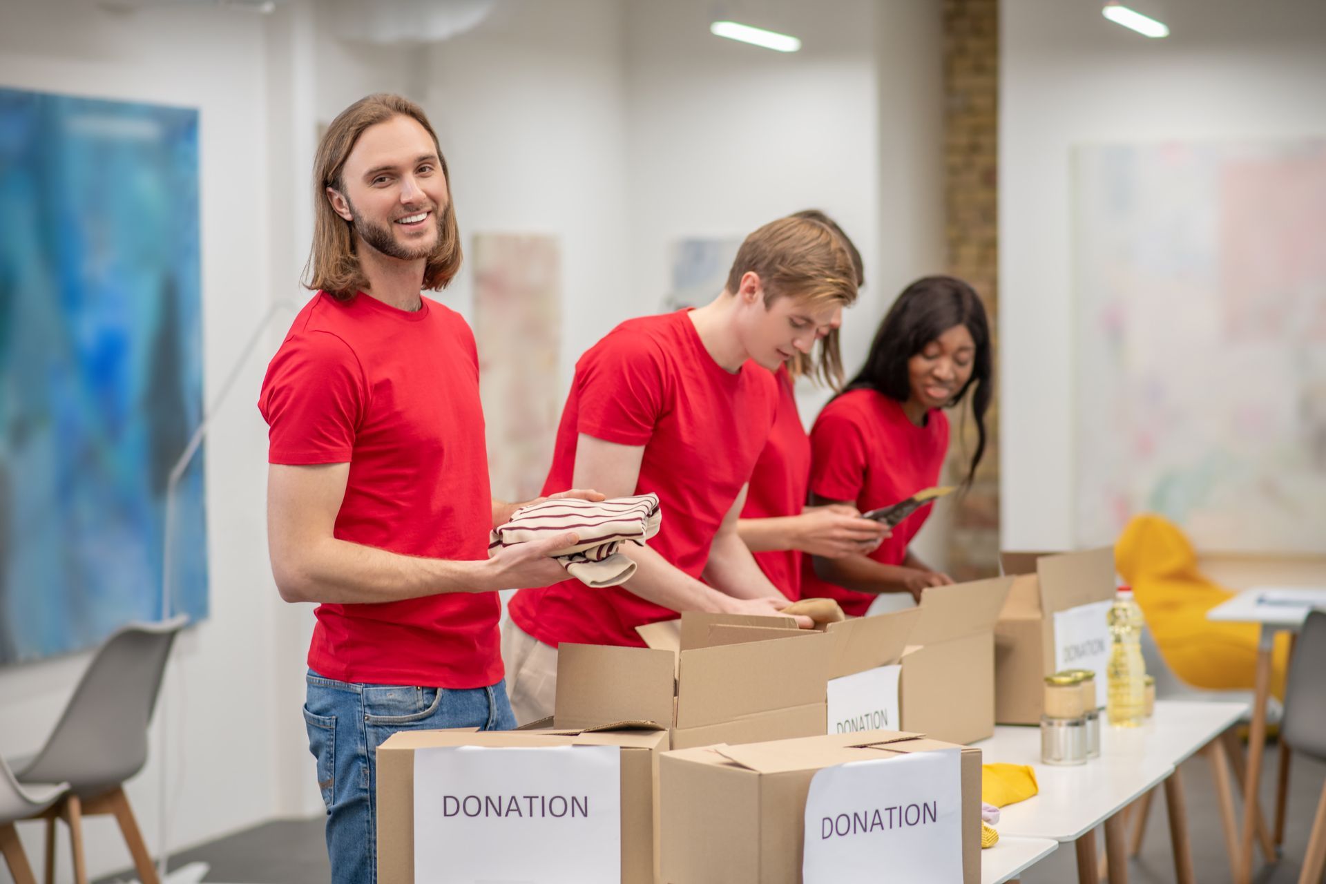 Three people wearing red shirts pack donations into boxes labeled