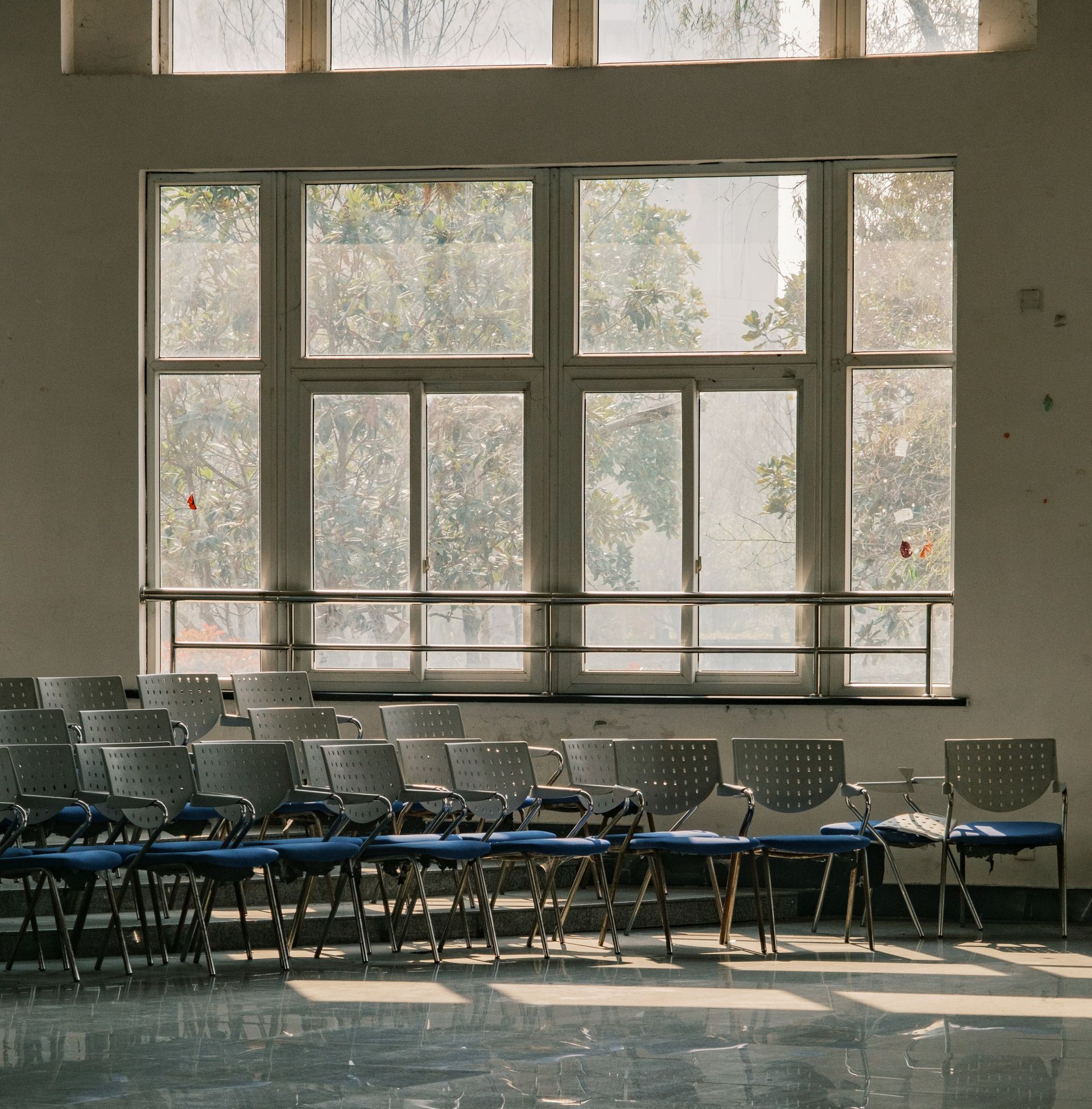 Rows of chairs face a large window in a classroom, sunlight streaming in.