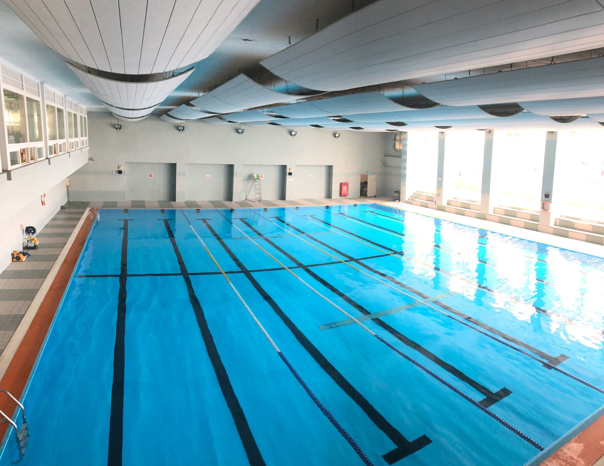 Indoor swimming pool with blue water and lanes. White ceiling and windows along one side.