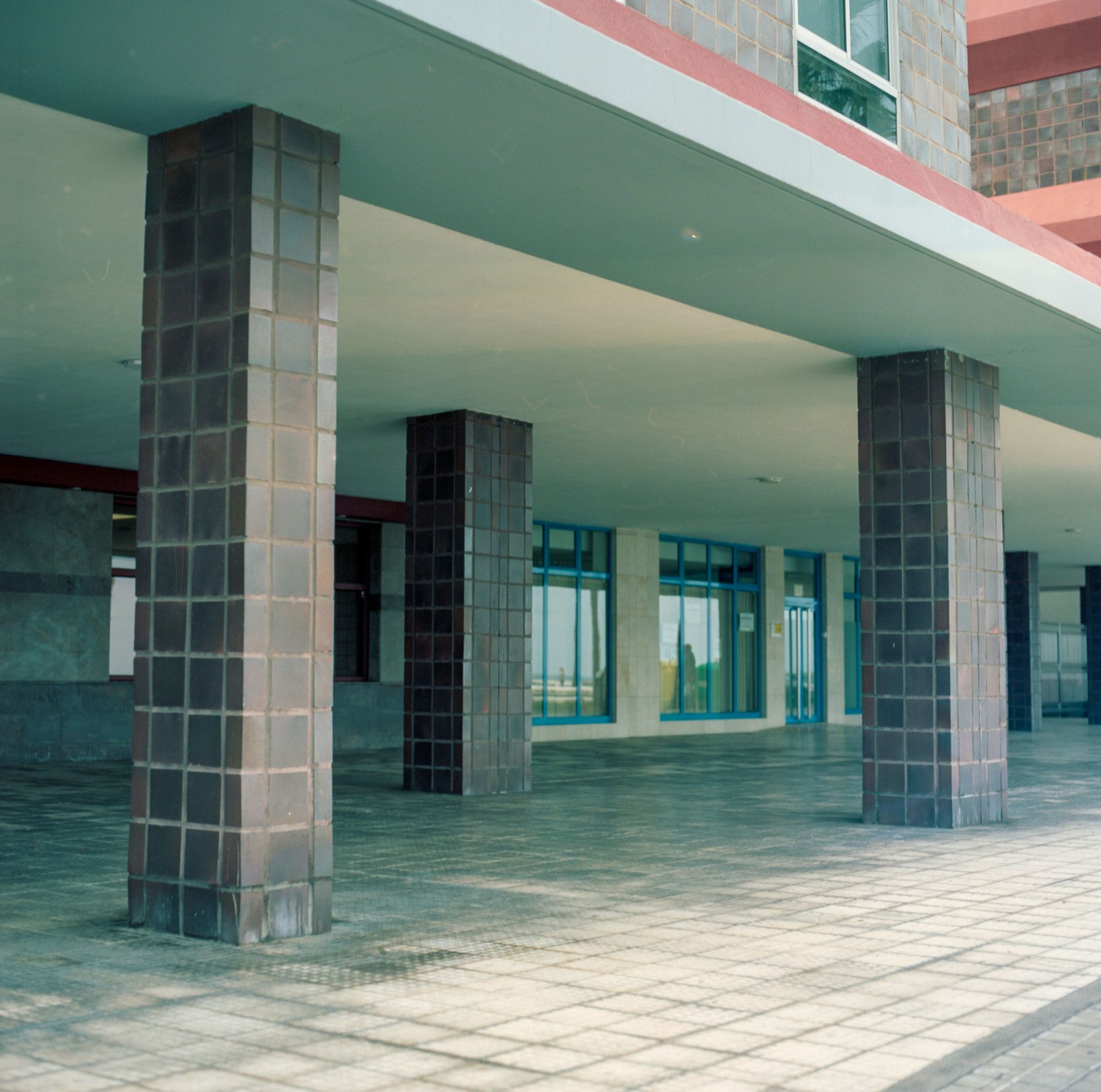 Covered walkway with tiled pillars supporting a building's roof; blue windows in the background.