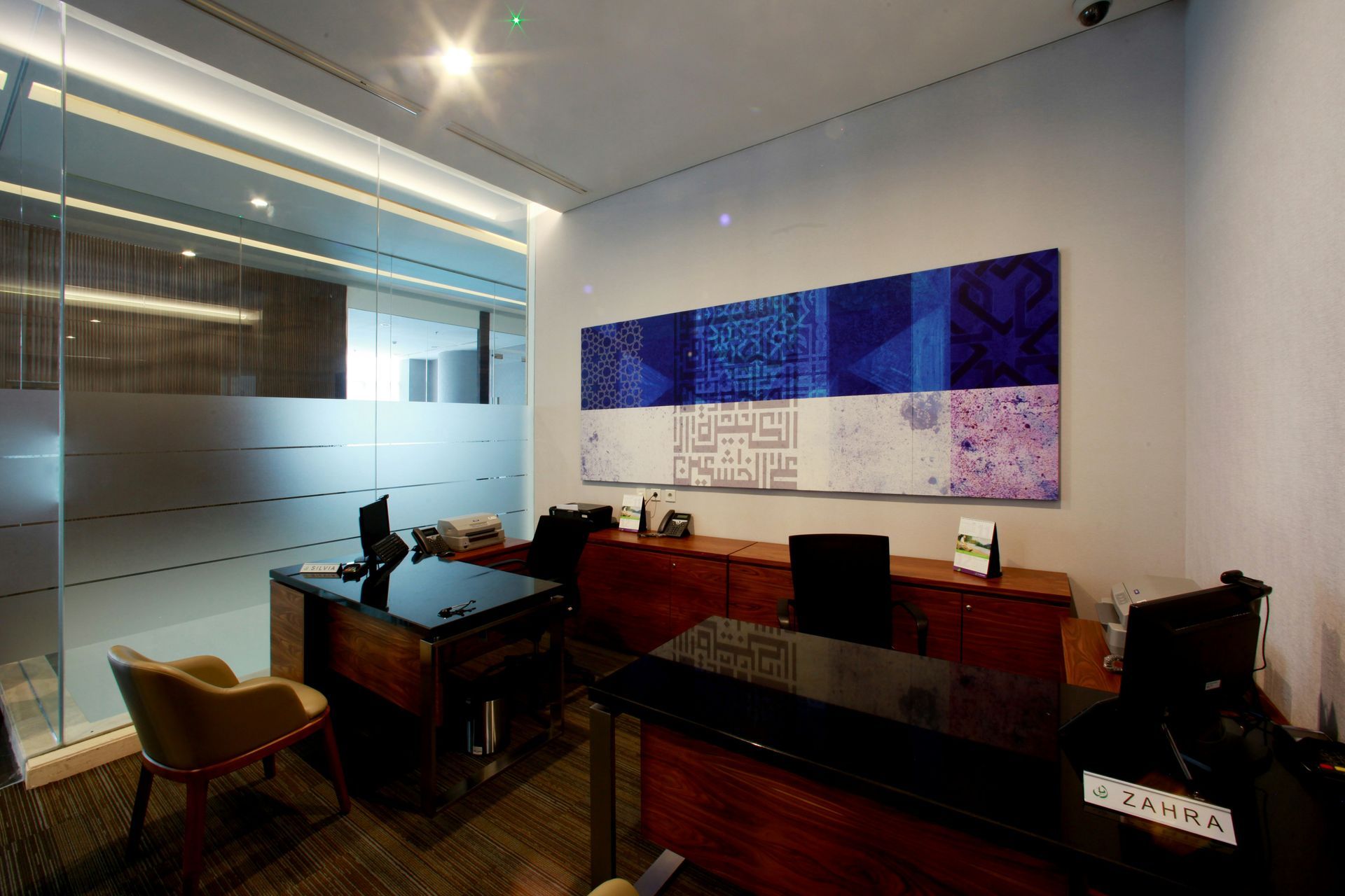Modern office with two desks, artwork, and a frosted glass wall.