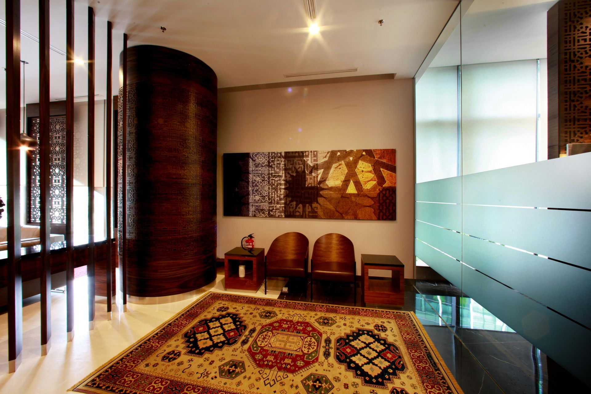 Lobby with patterned rug, curved wood panel, and wall art; frosted glass wall to the right.