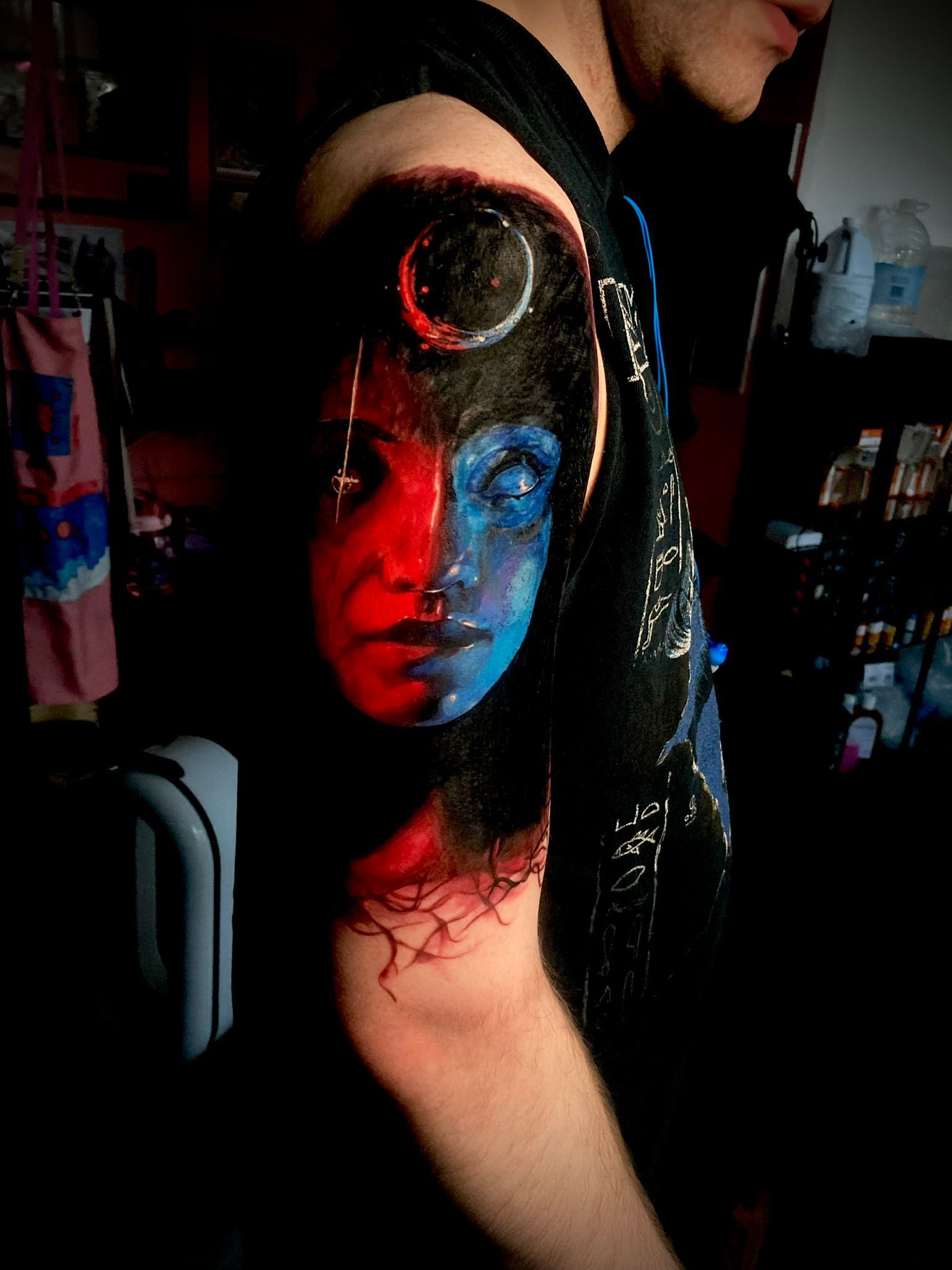 Half red, half blue face tattoo on an arm, with a celestial body and dark background.