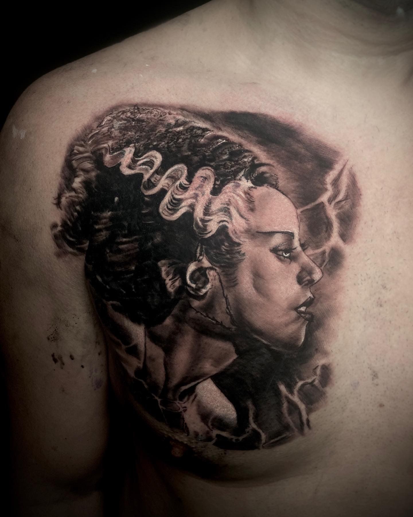 Black and grey tattoo of the Bride of Frankenstein on a person’s chest, detailed face and iconic hairstyle.
