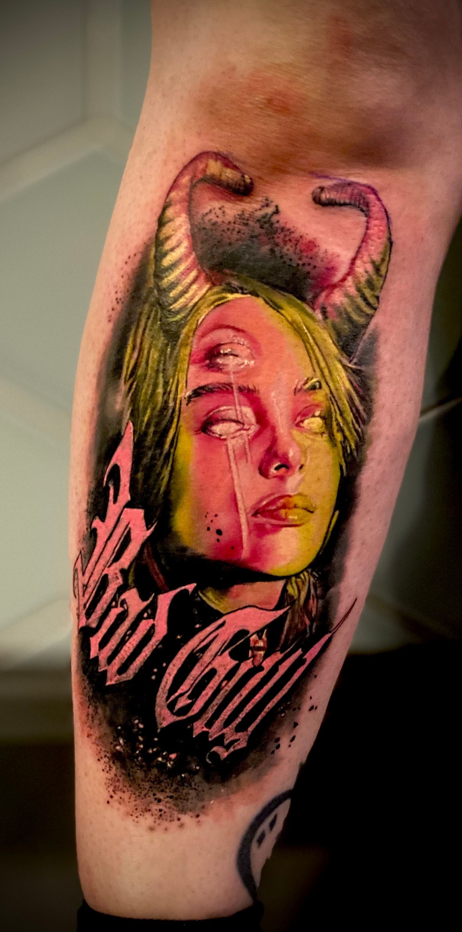 Tattoo on arm of a person: a demon-like face with horns and lettering 