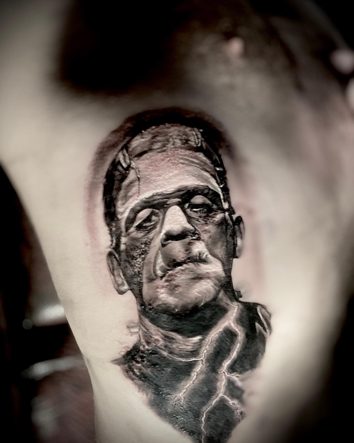 Frankenstein's monster tattoo on a person's side in black and gray. Features stitches, scars, and a dark shaded background.
